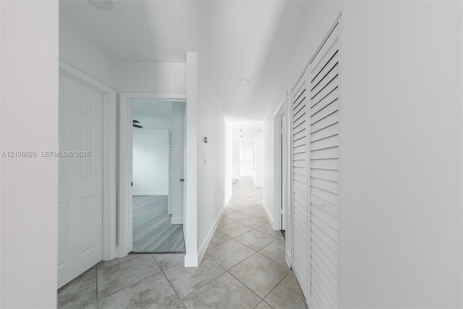 Hallway featuring neutral large-format tile flooring, louvered bi-fold closet doors, and recessed ceiling lighting