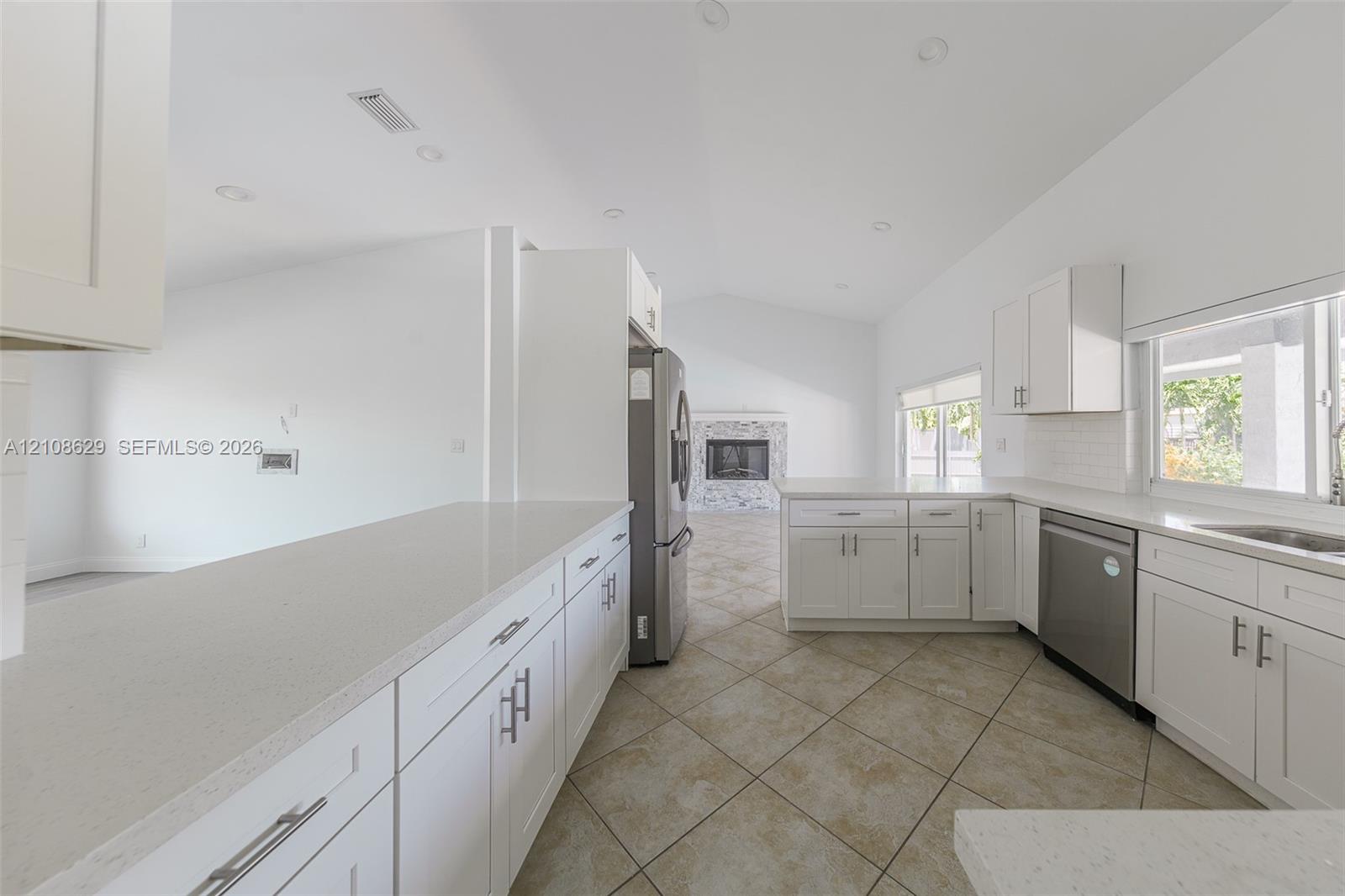 Kitchen featuring white shaker-style cabinetry, solid-surface countertops, tile flooring, stainless steel appliances, and recessed lighting