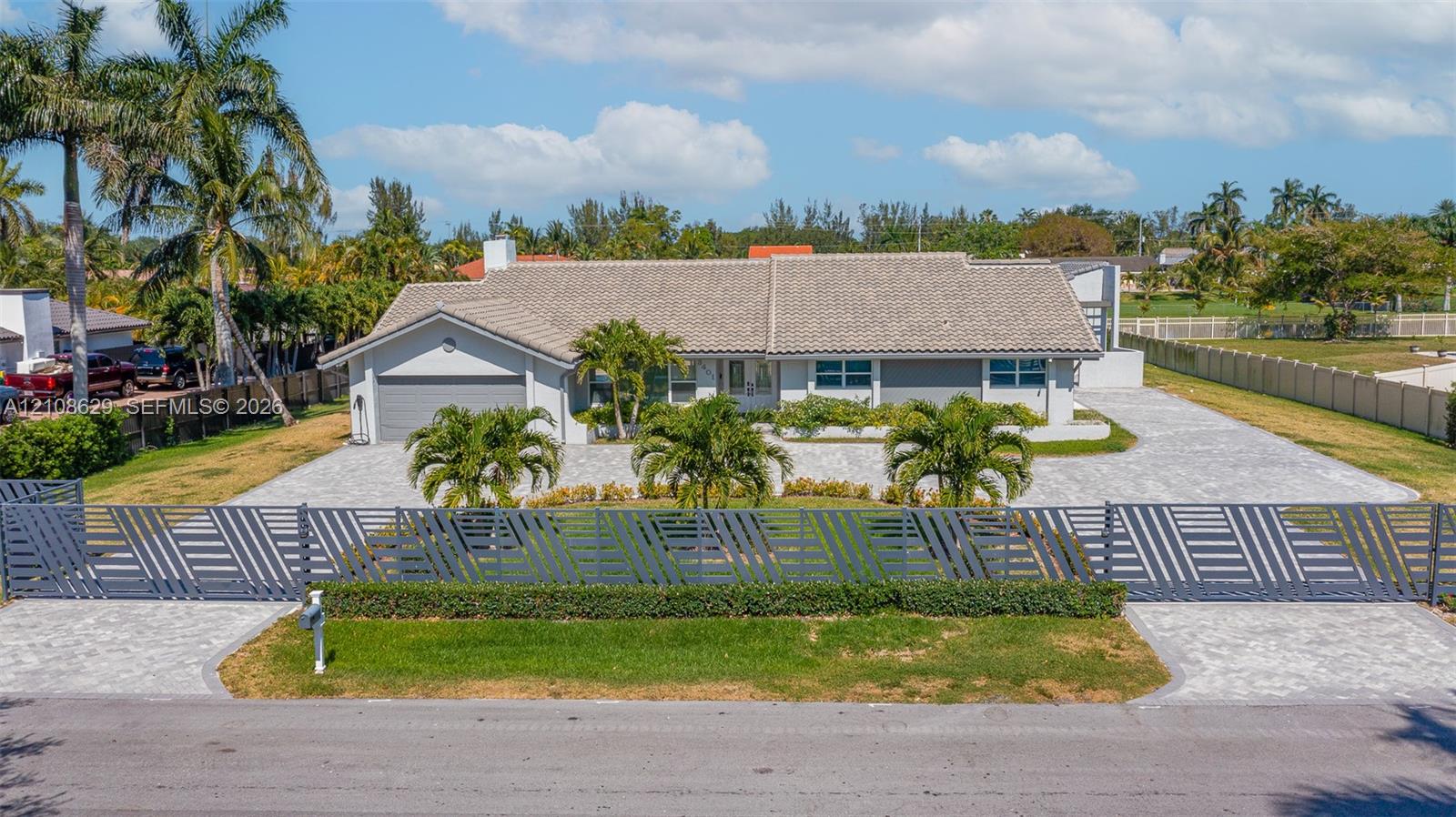Single-story exterior featuring a tile roof, an expansive paver driveway, and a gated perimeter entrance with contemporary horizontal slat fencing