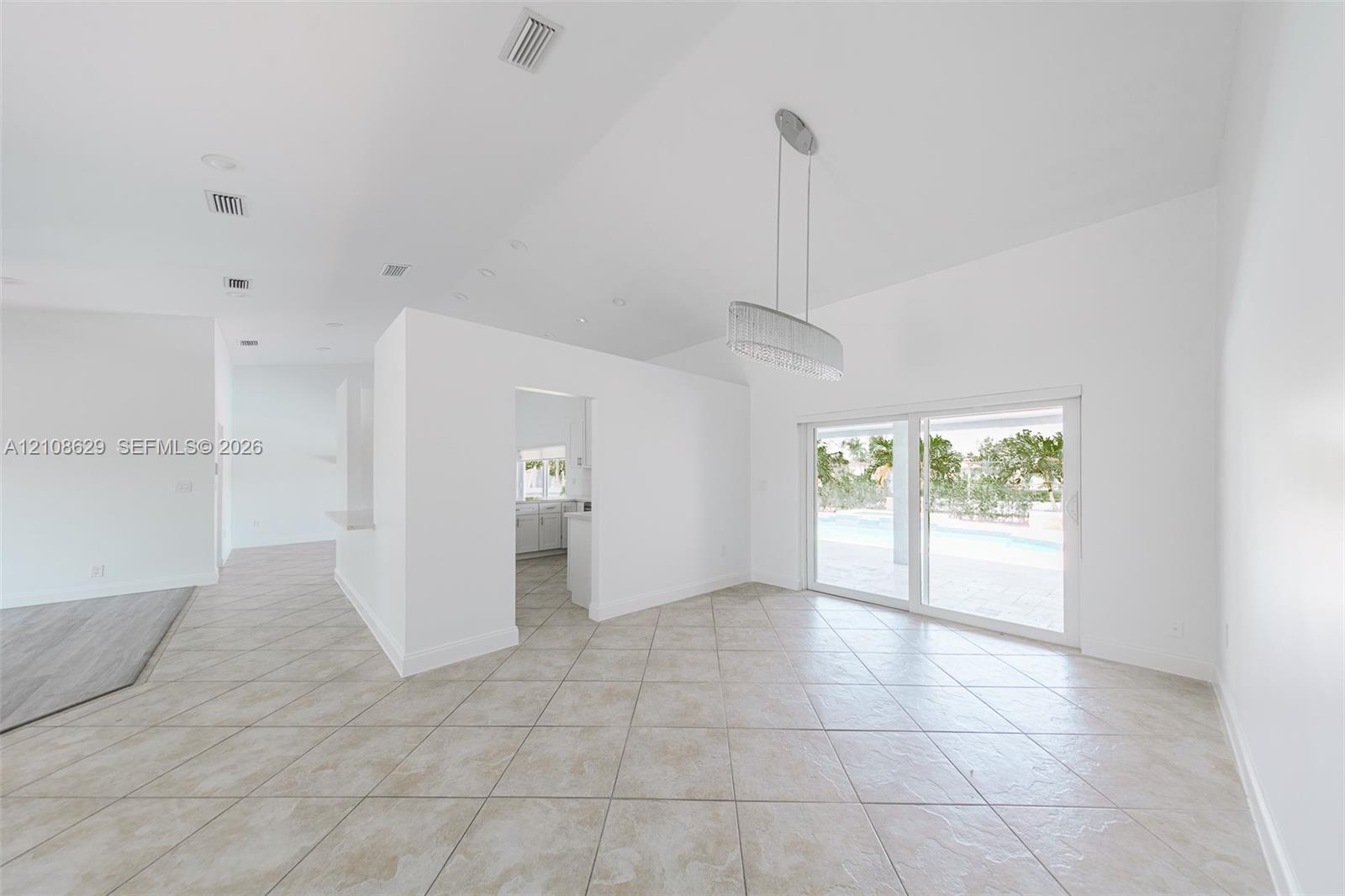 Open-concept interior featuring vaulted ceilings, oversized tile flooring, a contemporary linear chandelier, and sliding glass doors