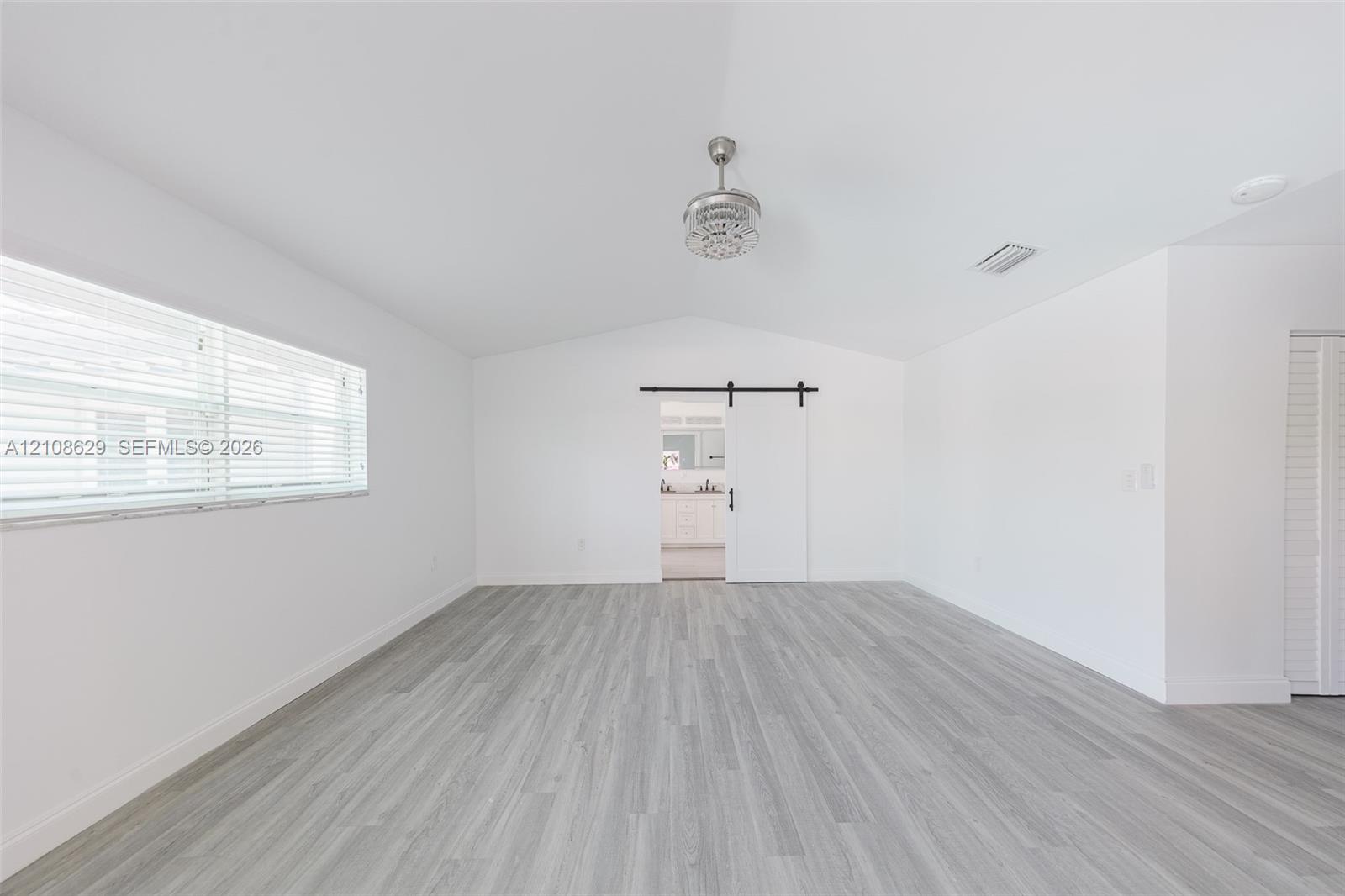 Spacious room showcasing gleaming wood-finish flooring, bright natural light from large windows, and clean white walls