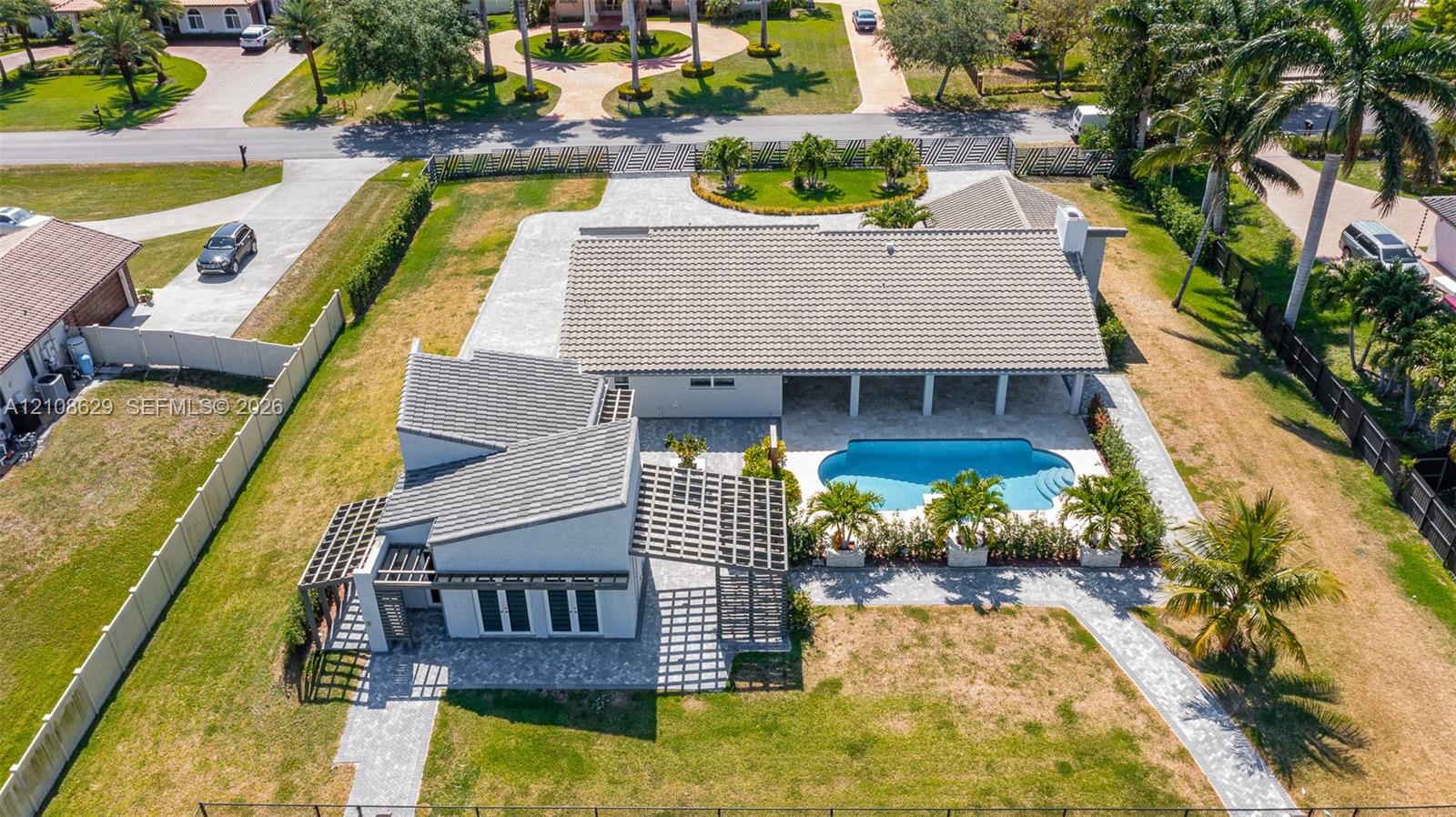 Aerial perspective of a multi-structure property featuring a swimming pool, covered patio, integrated wooden pergolas, and stone-paver hardscaping Aerial perspective of a multi-structure property featuring a swimming pool, covered patio, integrated wooden pergolas, and stone-paver hardscaping