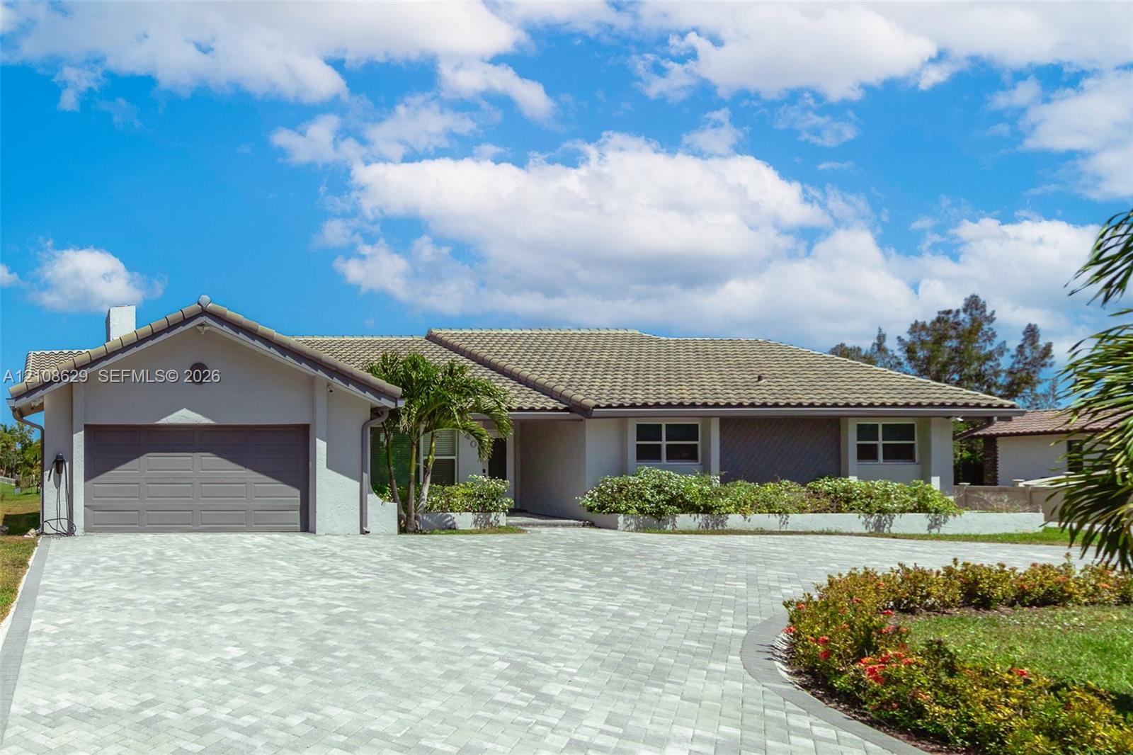 Single-story residence featuring a tile roof, light-toned exterior finish, paver driveway, and integrated garage