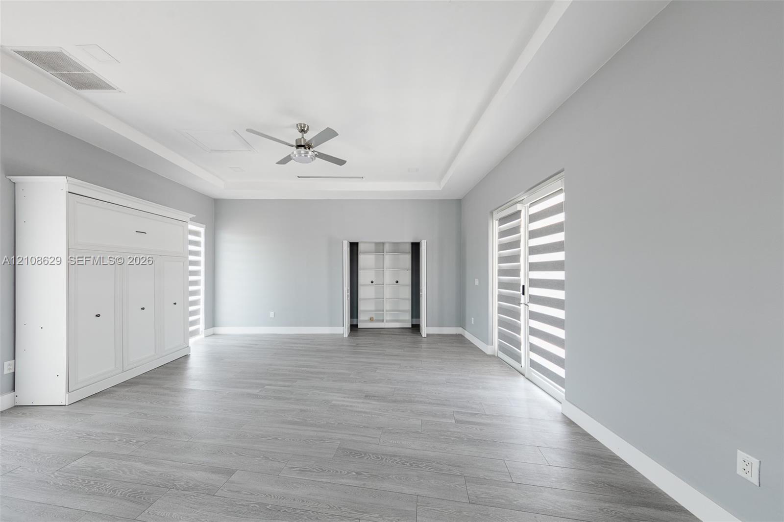 Tray ceiling with recessed lighting, integrated wall cabinetry, wood-finish flooring, ceiling fan with light fixture, and floor-to-ceiling glass sliding doors