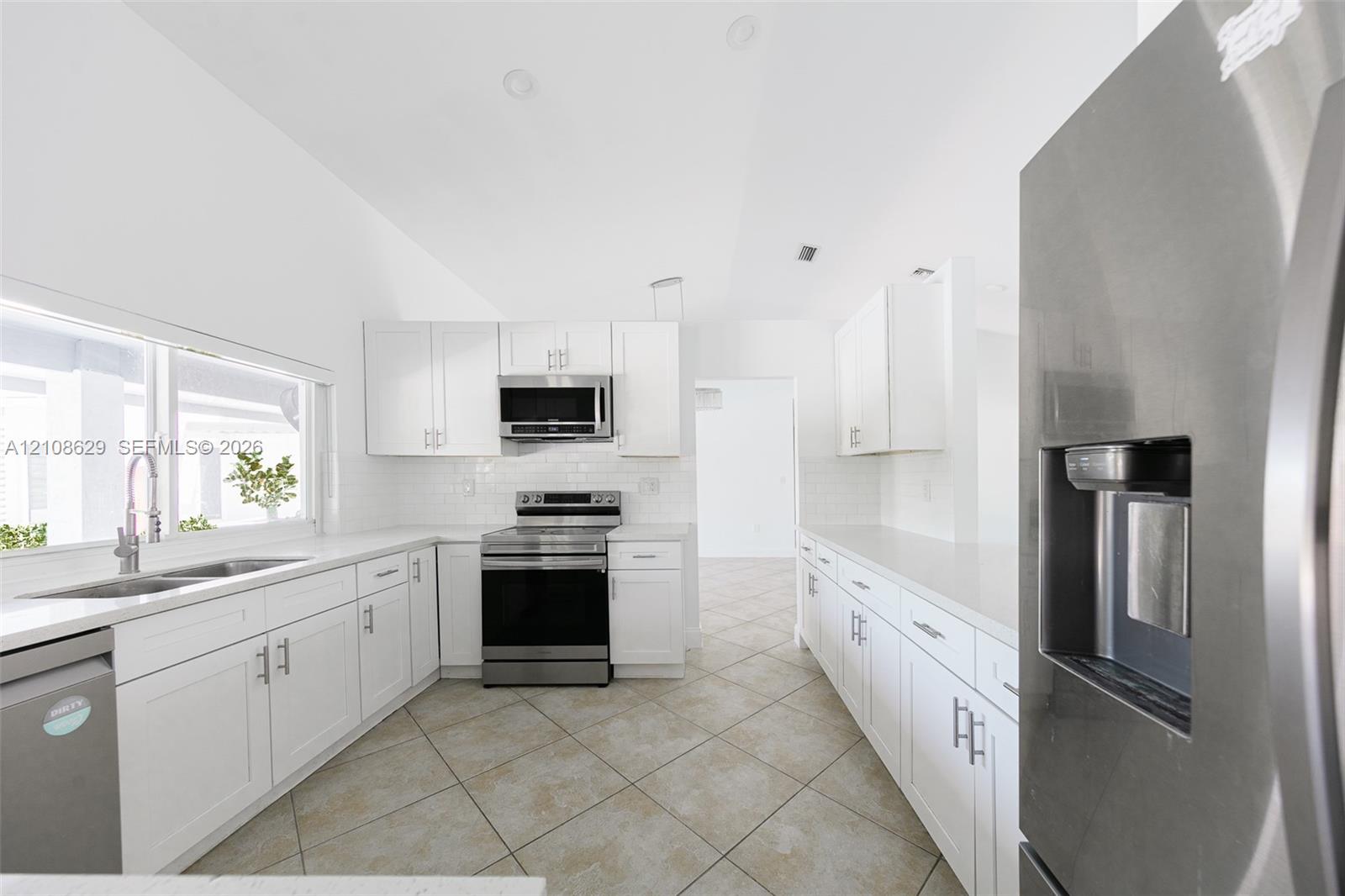 Kitchen featuring white cabinetry, solid-surface countertops, tile flooring, stainless steel appliances, and a double-basin sink