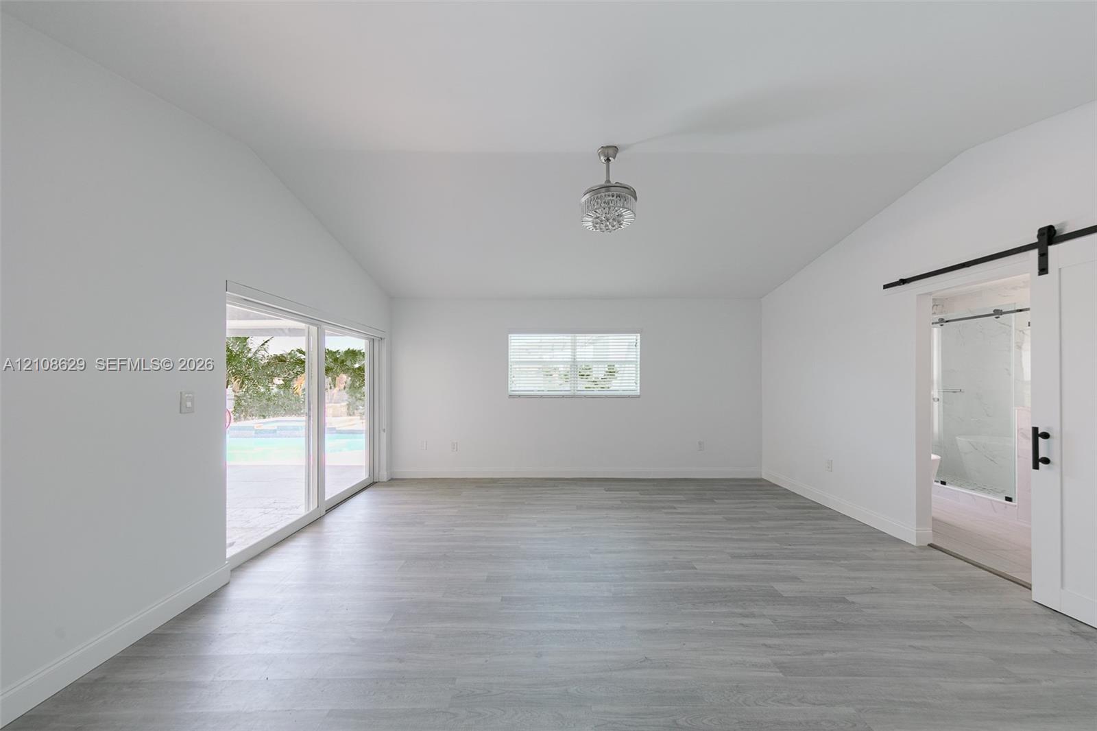 Vaulted ceilings with a centralized ceiling fan, wood-finish flooring, sliding glass doors, and a sliding barn-style door