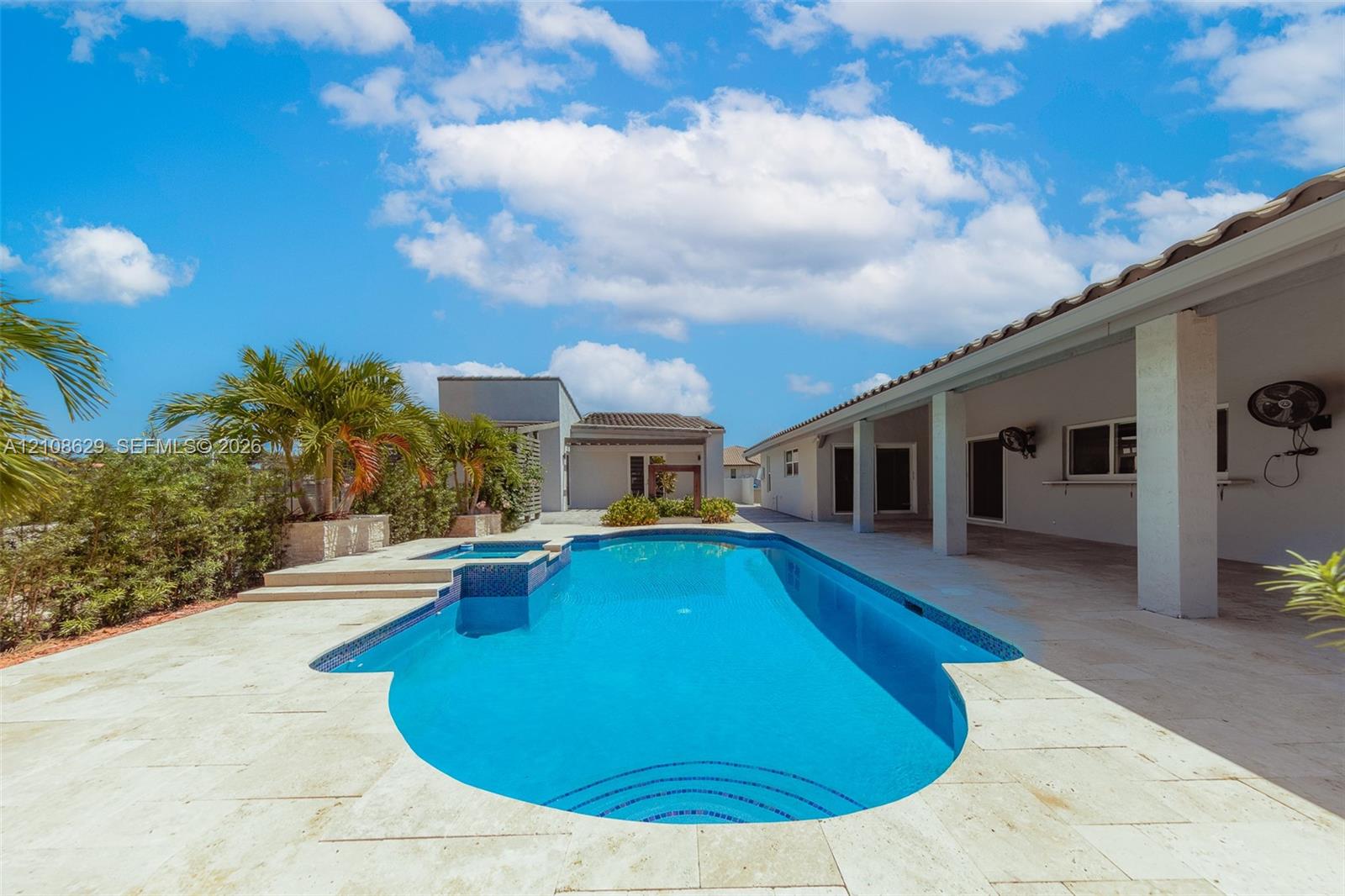 Swimming pool with integrated spa, stone paver decking, covered patio, and mature palm trees