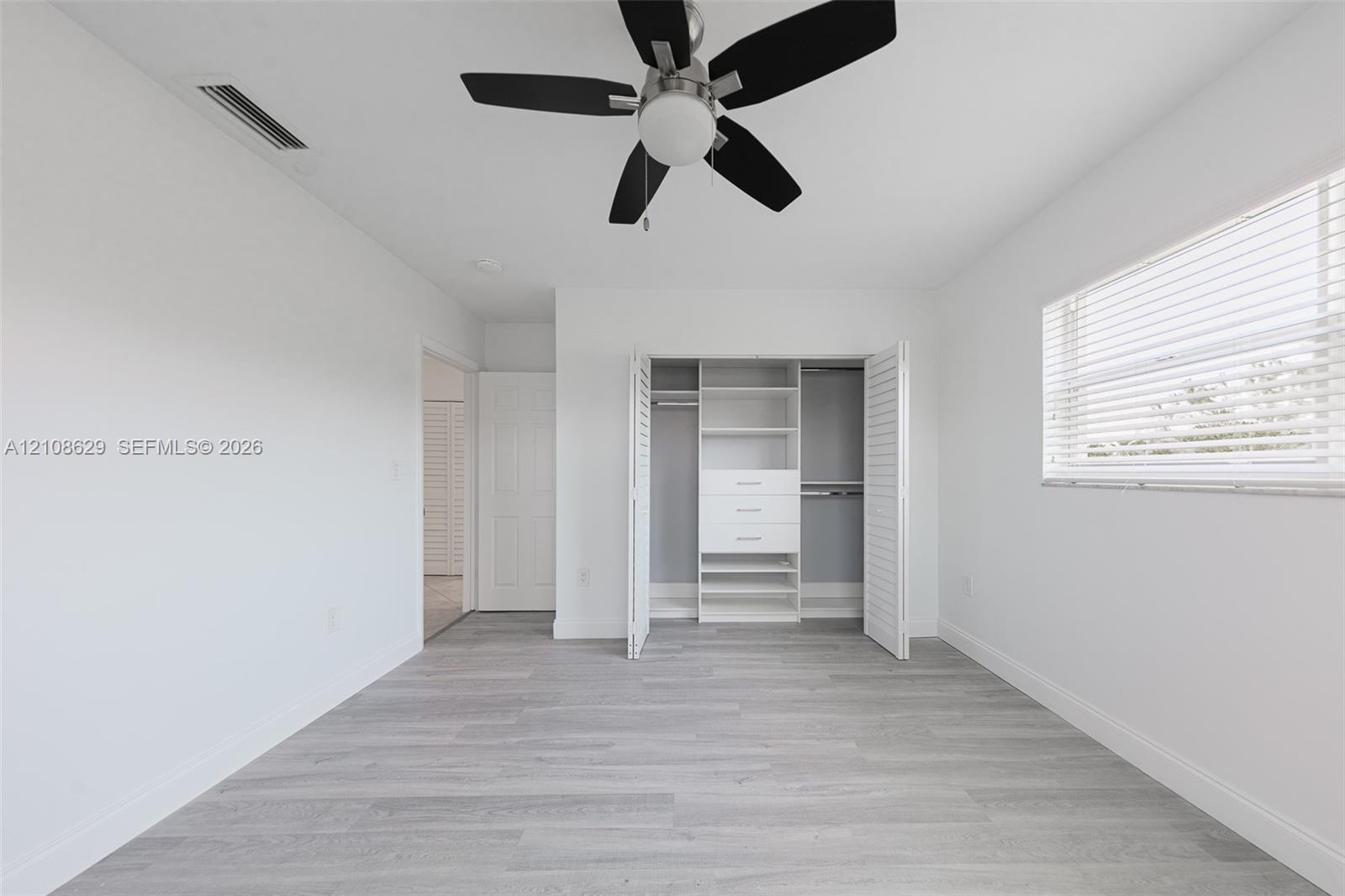 Neutral-toned interior featuring wood-finish flooring, a ceiling fan with integrated lighting, and a closet with custom built-in shelving and drawer storage