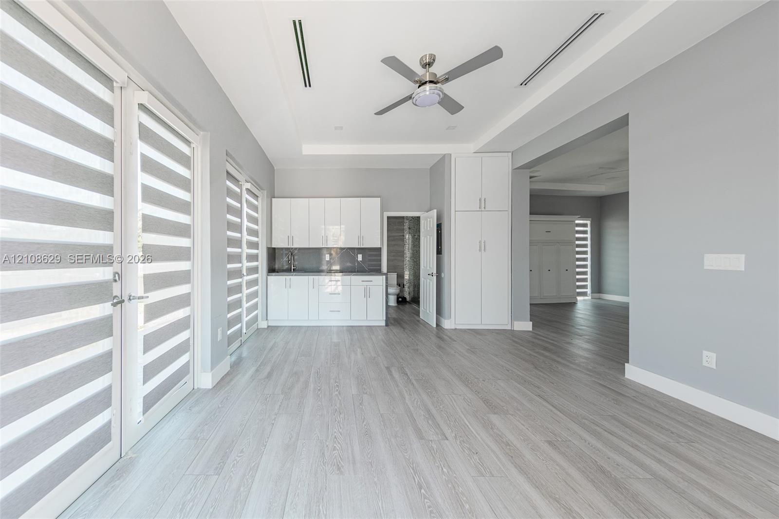 Interior space featuring wood-finish flooring, tray ceiling with a central ceiling fan, built-in white cabinetry, and dual glass-panel doors with integrated blinds