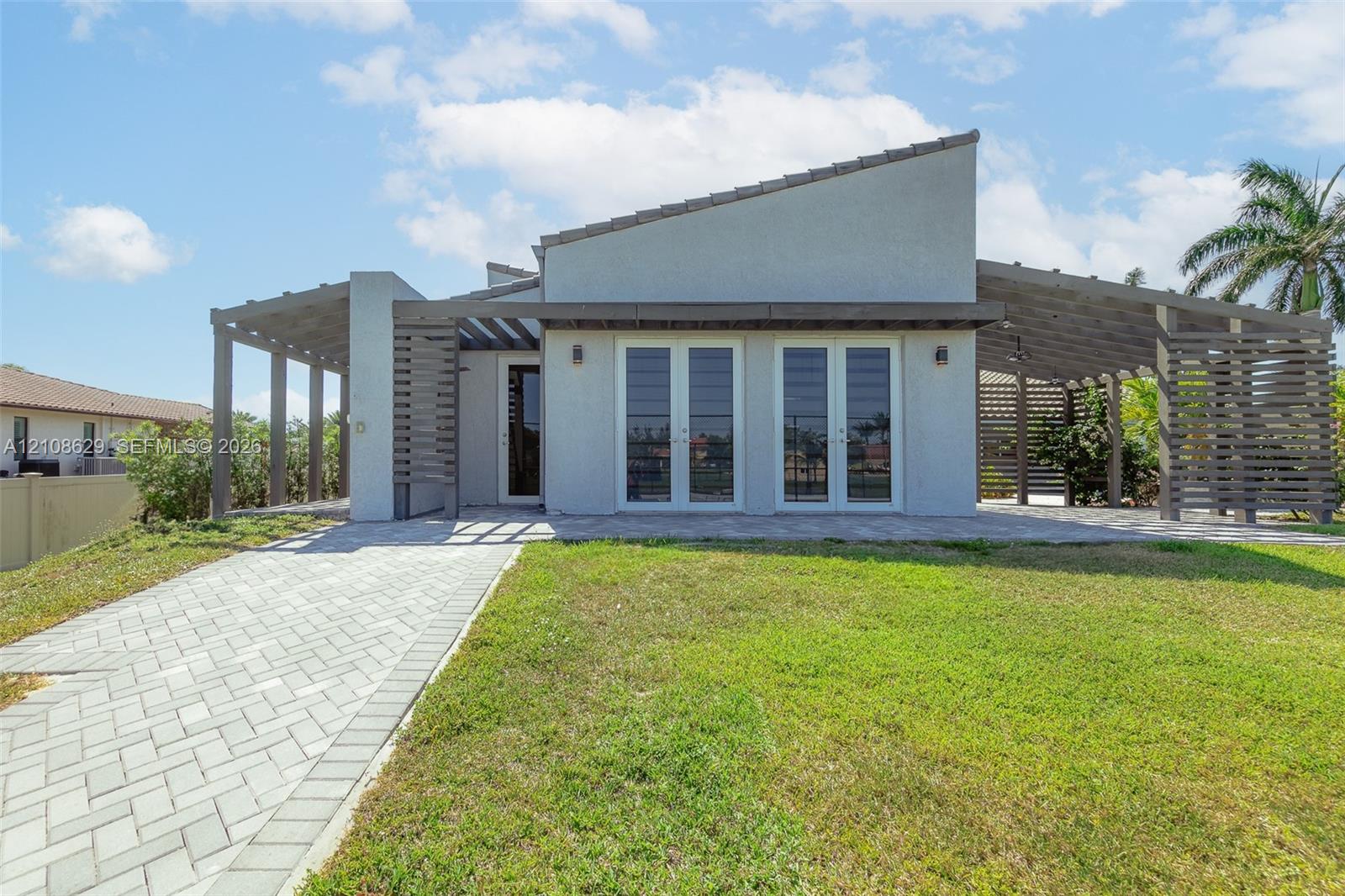 Modern exterior featuring a shed-style roofline, dual wood-finish pergolas, paver hardscaping, and double glass-paned doors