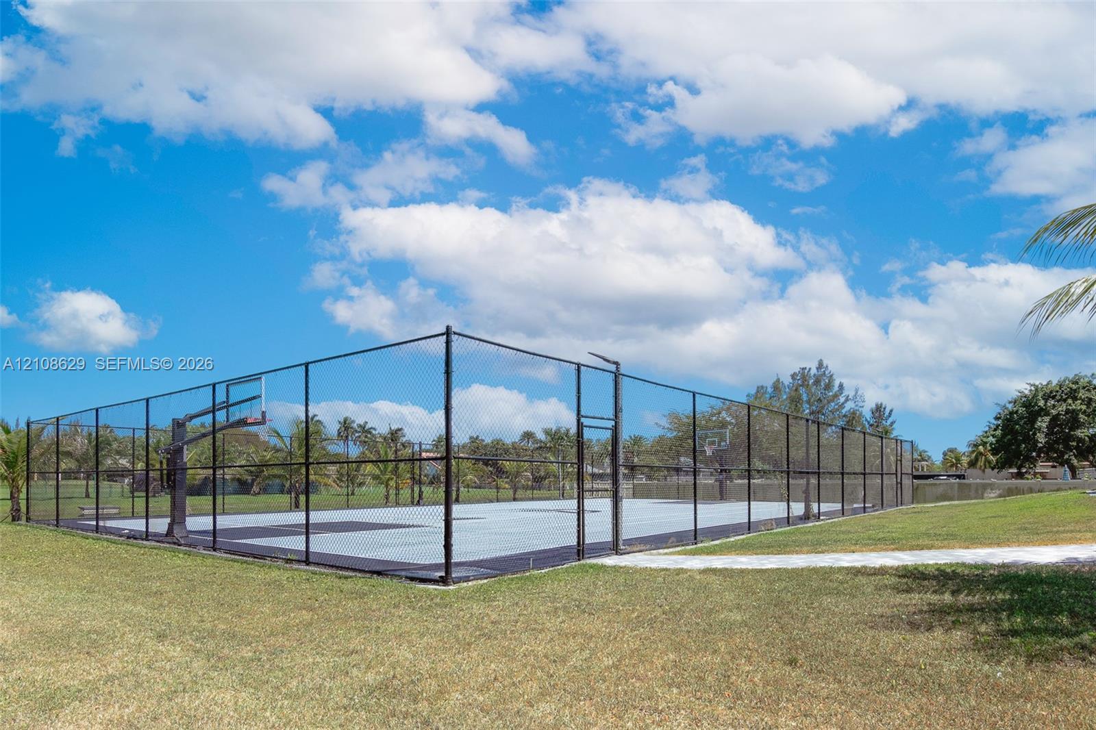 Outdoor sports court featuring a paved surface, dual built-in basketball hoops, and full perimeter chain-link fencing