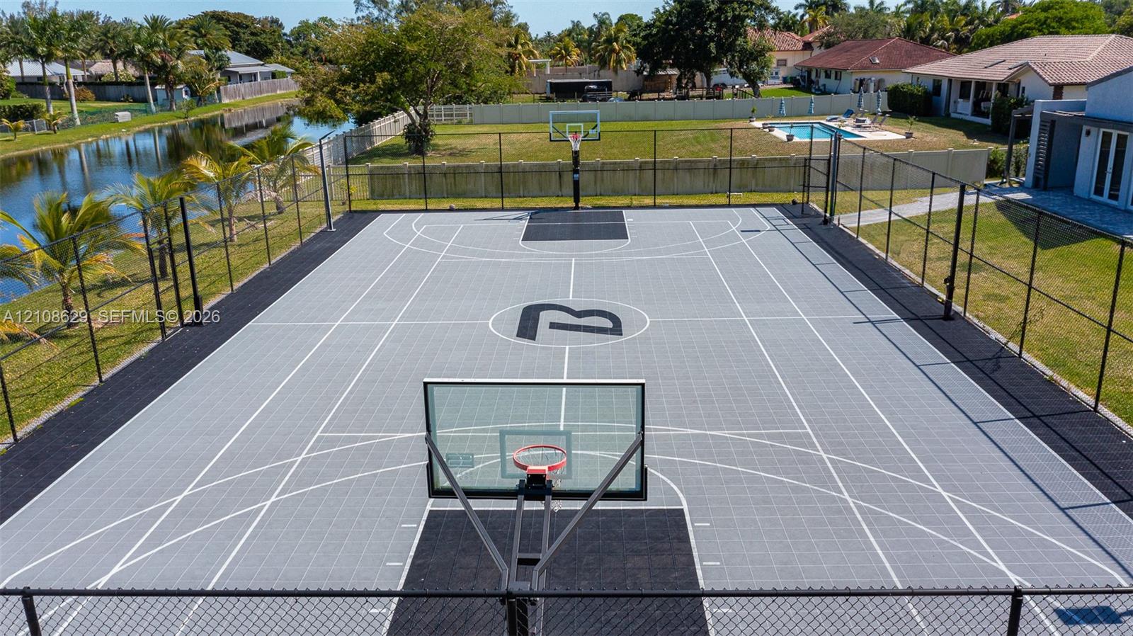 Private outdoor basketball court featuring interlocking modular surface tiles, perimeter chain-link fencing, and dual glass backboards with metal rims