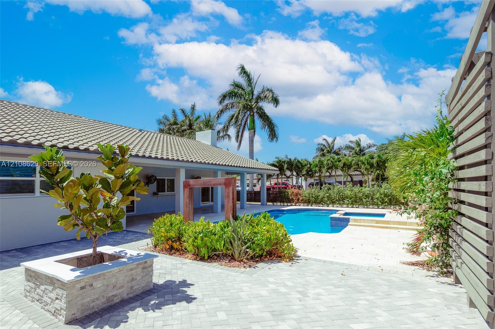 Rear exterior featuring a paver patio, stone-veneer planter, swimming pool with integrated spa, and a covered lanai
