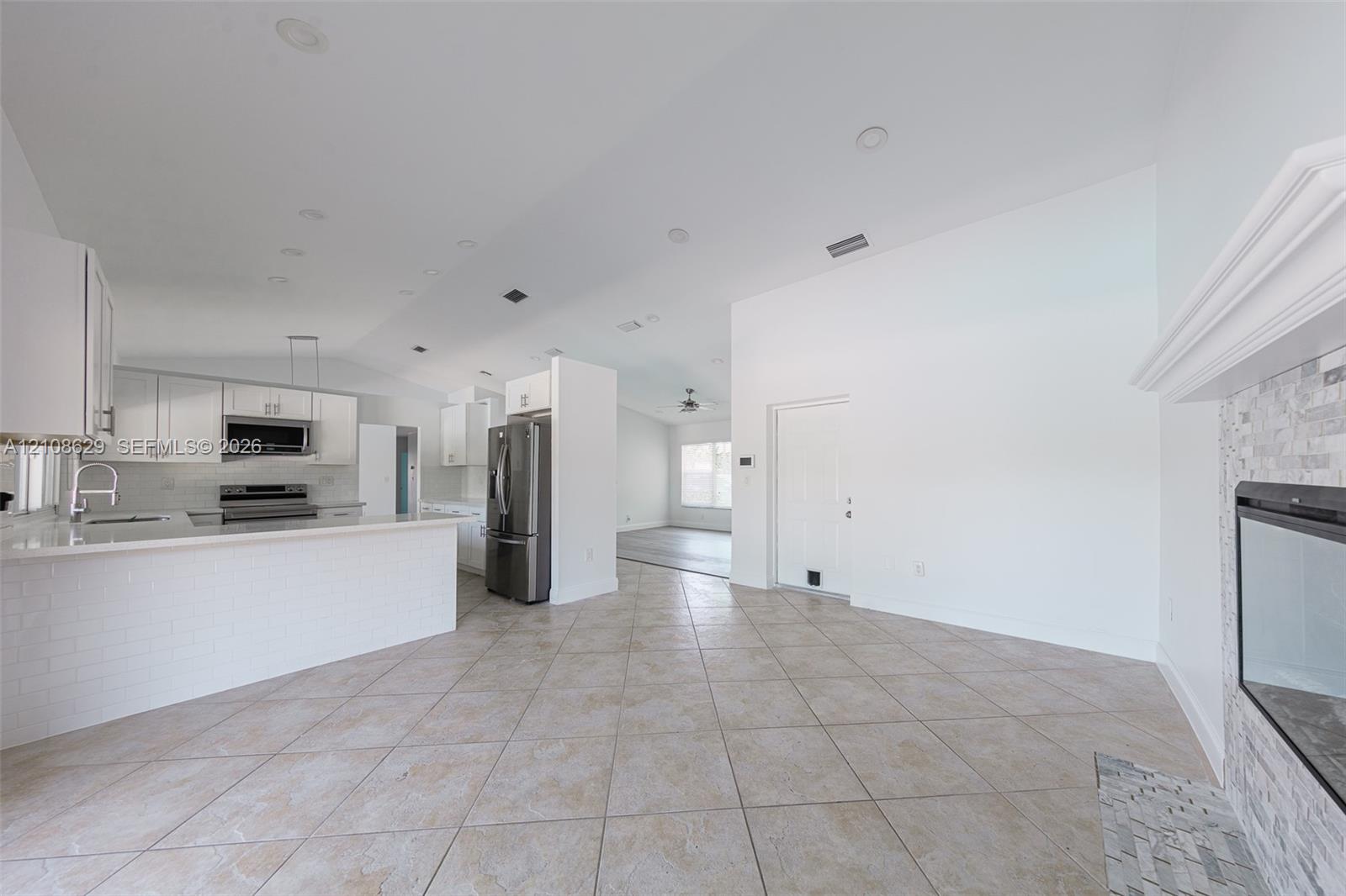 Kitchen featuring white shaker-style cabinetry, a stone tile backsplash, a peninsula with a quartz countertop, tile flooring, and a fireplace with a stone veneer surround