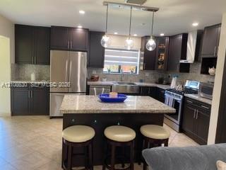 Kitchen featuring dark cabinetry, a central island with stone-finish countertops, a stainless steel apron-front sink, recessed lighting, and a triple-pendant fixture Kitchen featuring dark cabinetry, a central island with stone-finish countertops, a stainless steel apron-front sink, recessed lighting, and a triple-pendant fixture
