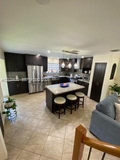 Kitchen featuring dark-toned cabinetry, stainless steel appliances, stone-surface countertops, central island, and ceramic tile flooring Kitchen featuring dark-toned cabinetry, stainless steel appliances, stone-surface countertops, central island, and ceramic tile flooring