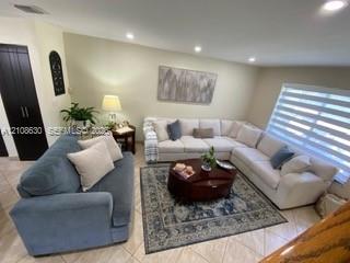 Living area featuring large-format ceramic tile flooring, recessed ceiling lighting, and horizontal window shades