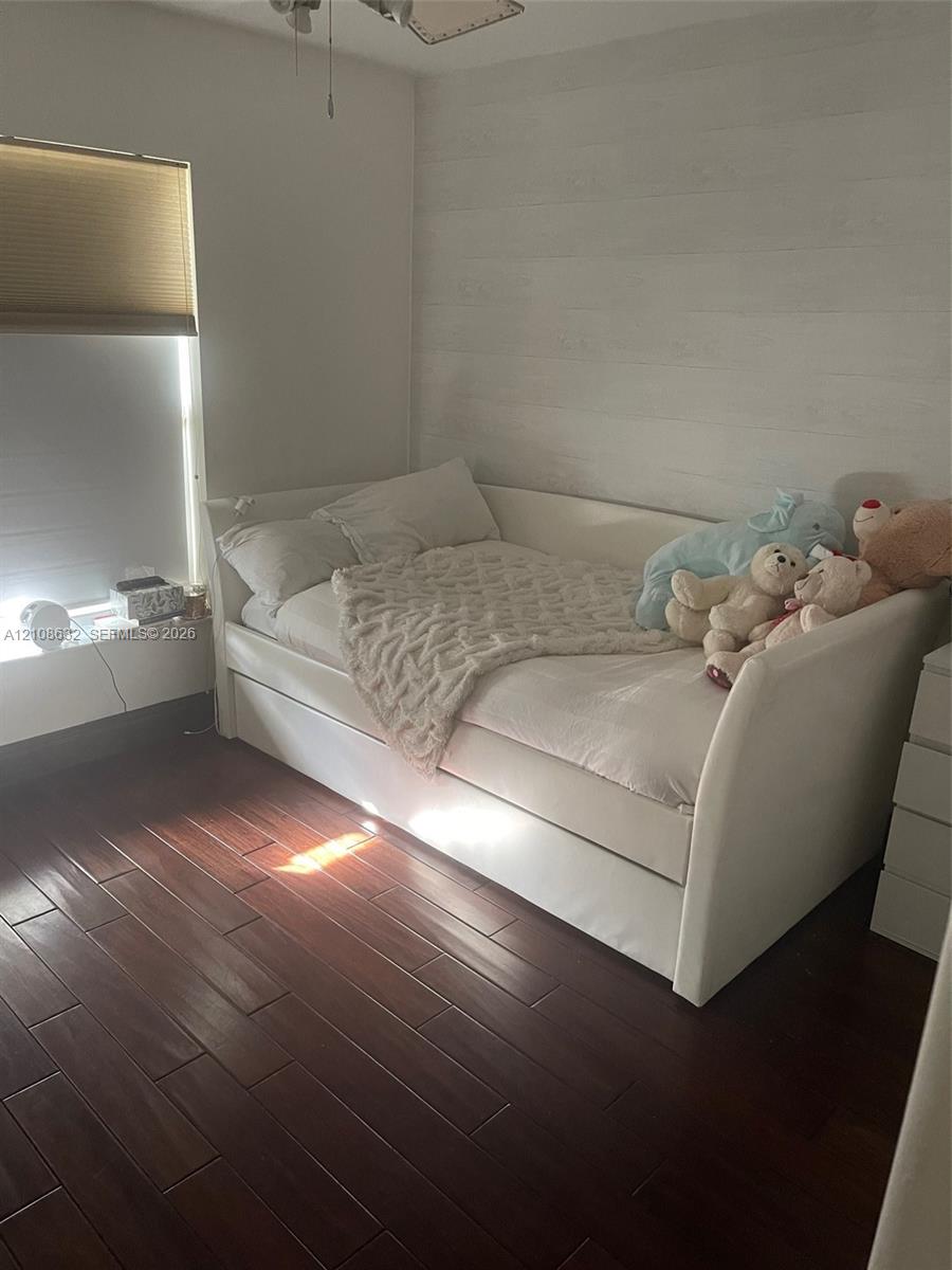 Room featuring dark-toned wood-finish flooring, white horizontal shiplap wall detail, and a ceiling fan with integrated lighting