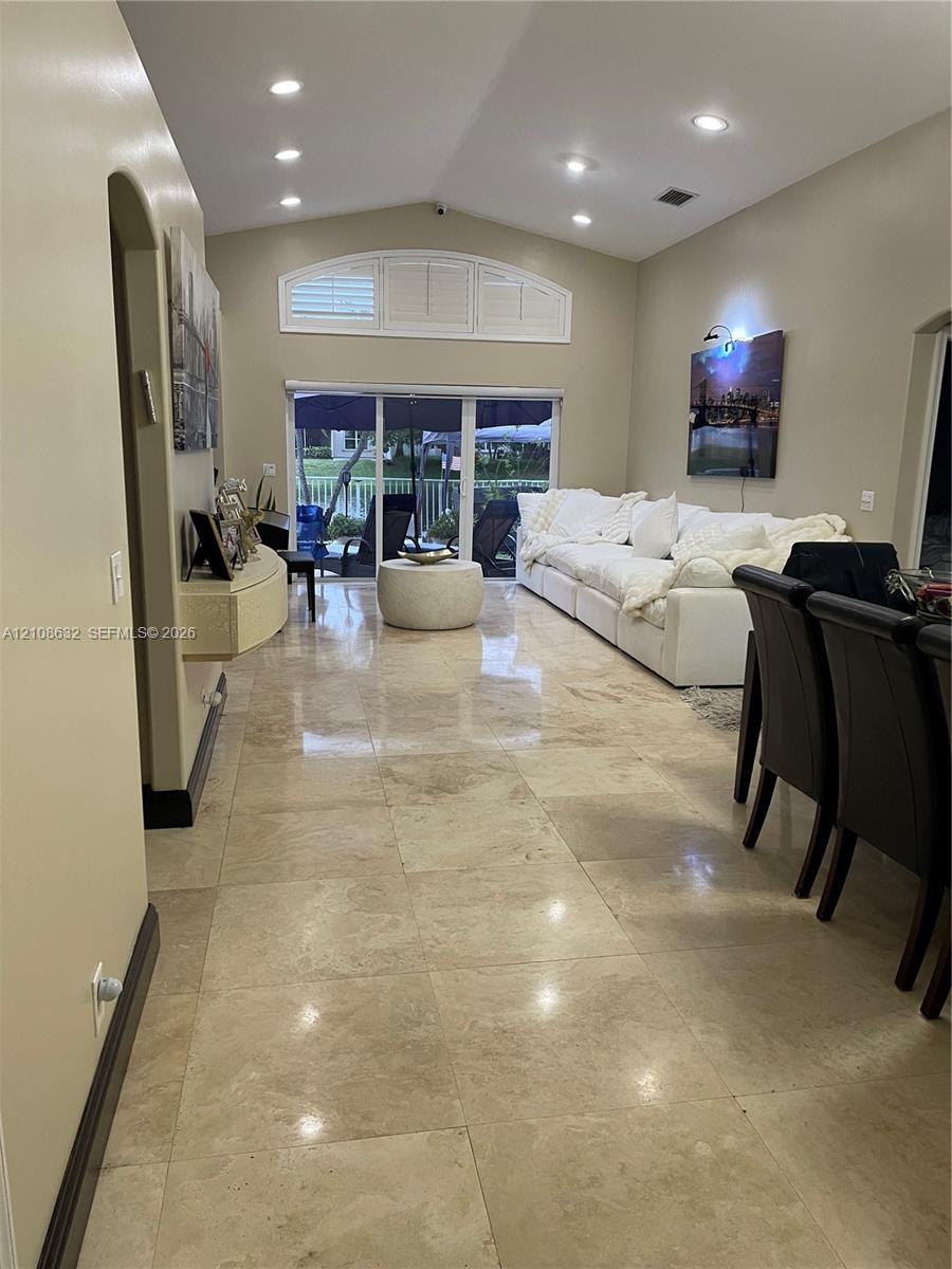 Spacious interior featuring large-format stone-style tile flooring, vaulted ceilings, recessed lighting, and an arched transom window above glass sliding doors Spacious interior featuring large-format stone-style tile flooring, vaulted ceilings, recessed lighting, and an arched transom window above glass sliding doors