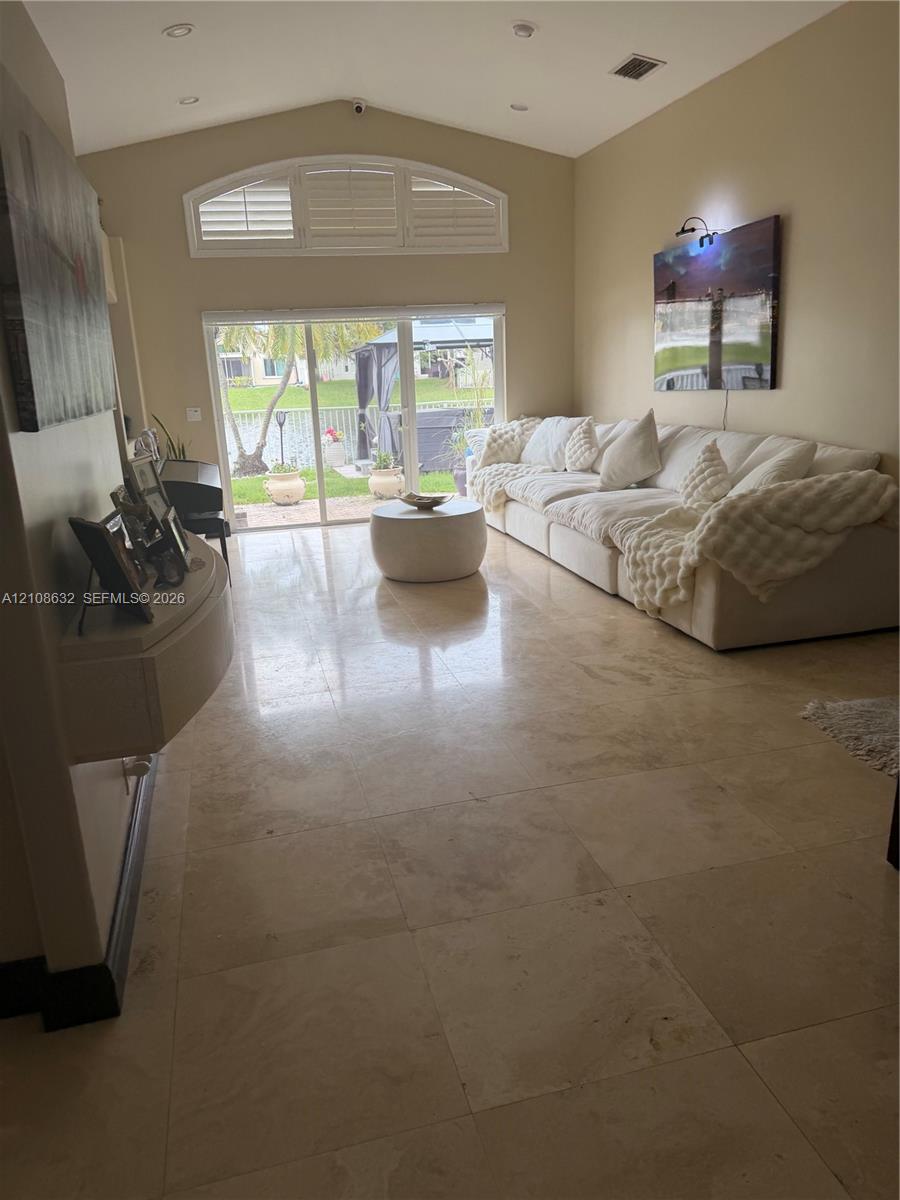 Vaulted ceiling featuring recessed lighting, large-format stone tile flooring, arched clerestory window, and sliding glass doors