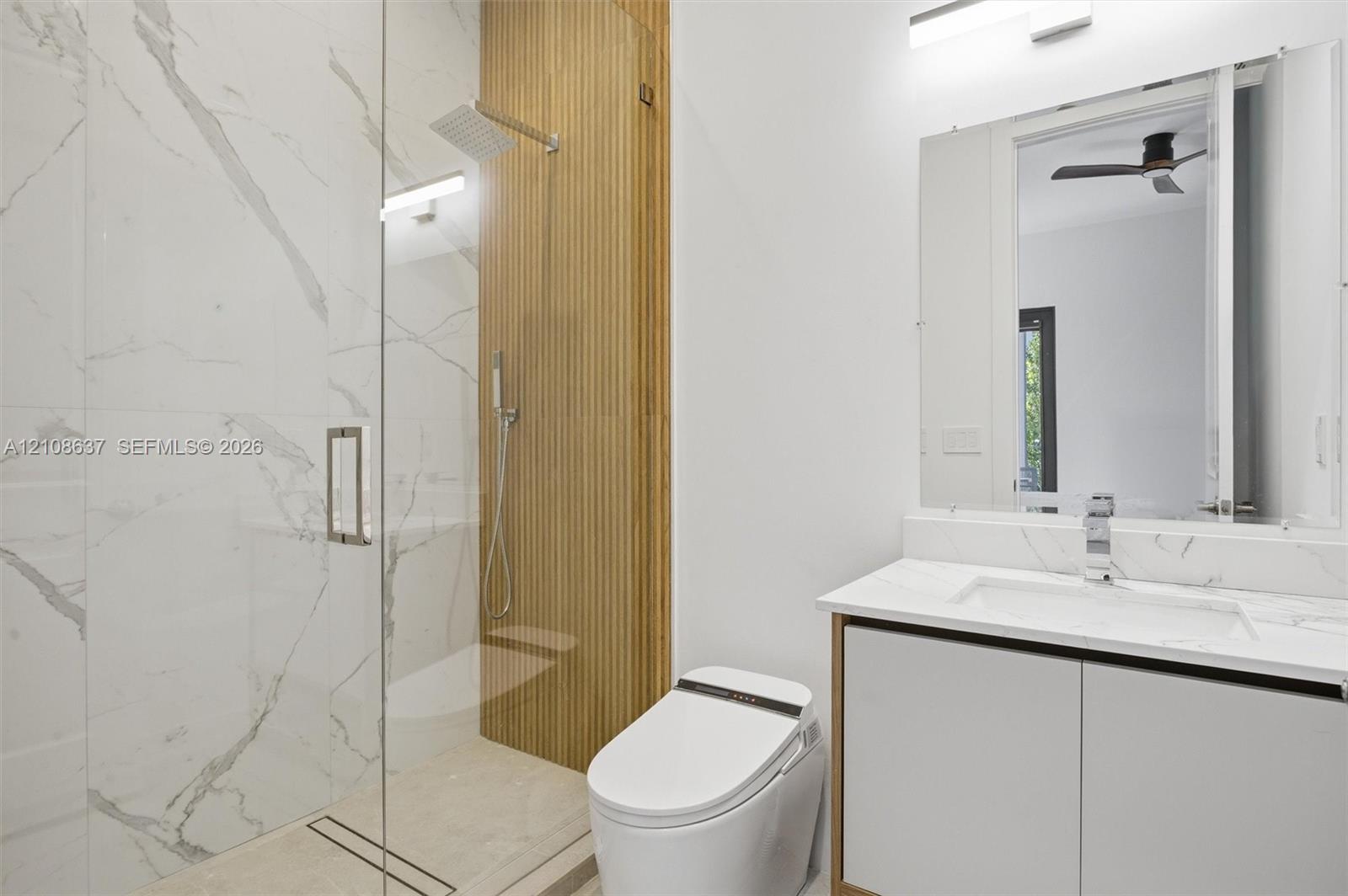 Walk-in shower with floor-to-ceiling stone-patterned tile, vertical wood-slat accent wall, rainfall showerhead, glass enclosure, and floating vanity with integrated countertop and sink