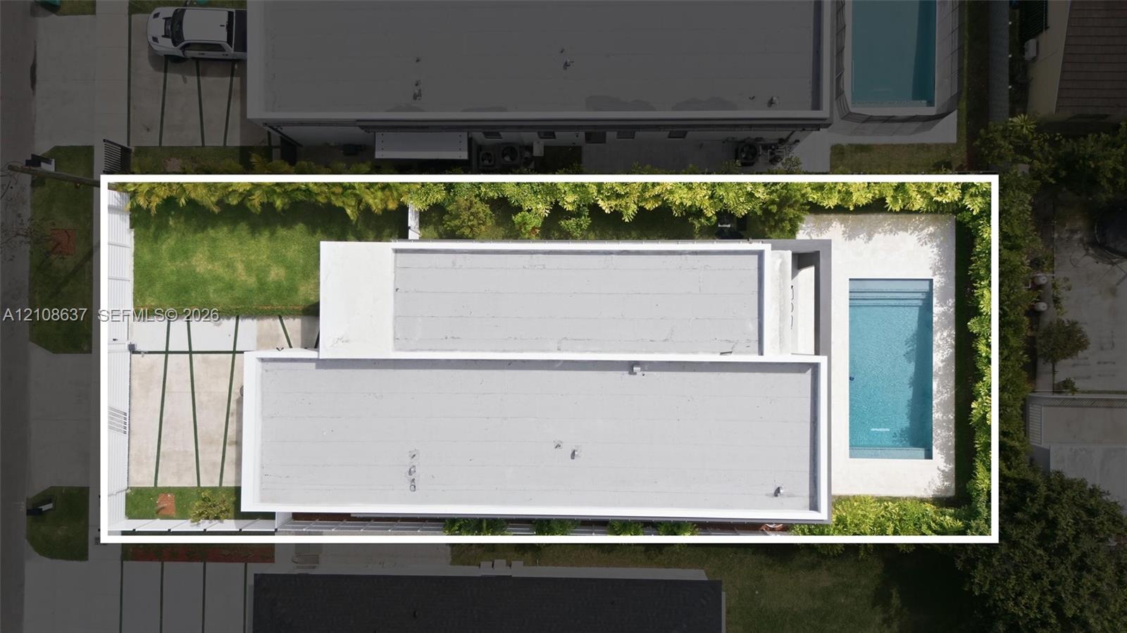 Aerial perspective of property exterior featuring a swimming pool, concrete hardscaping with grass inlays, and perimeter privacy hedging