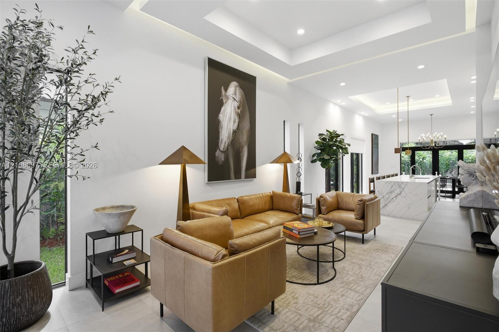 Open-concept living space featuring high ceilings with integrated tray lighting, full-height windows, recessed lighting, and a stone-clad kitchen island