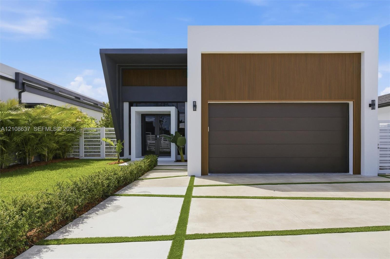 Modern architectural exterior featuring clean white stucco, charcoal grey framing, wood-finish paneling, and a segmented concrete driveway with grass inlays Modern architectural exterior featuring clean white stucco, charcoal grey framing, wood-finish paneling, and a segmented concrete driveway with grass inlays