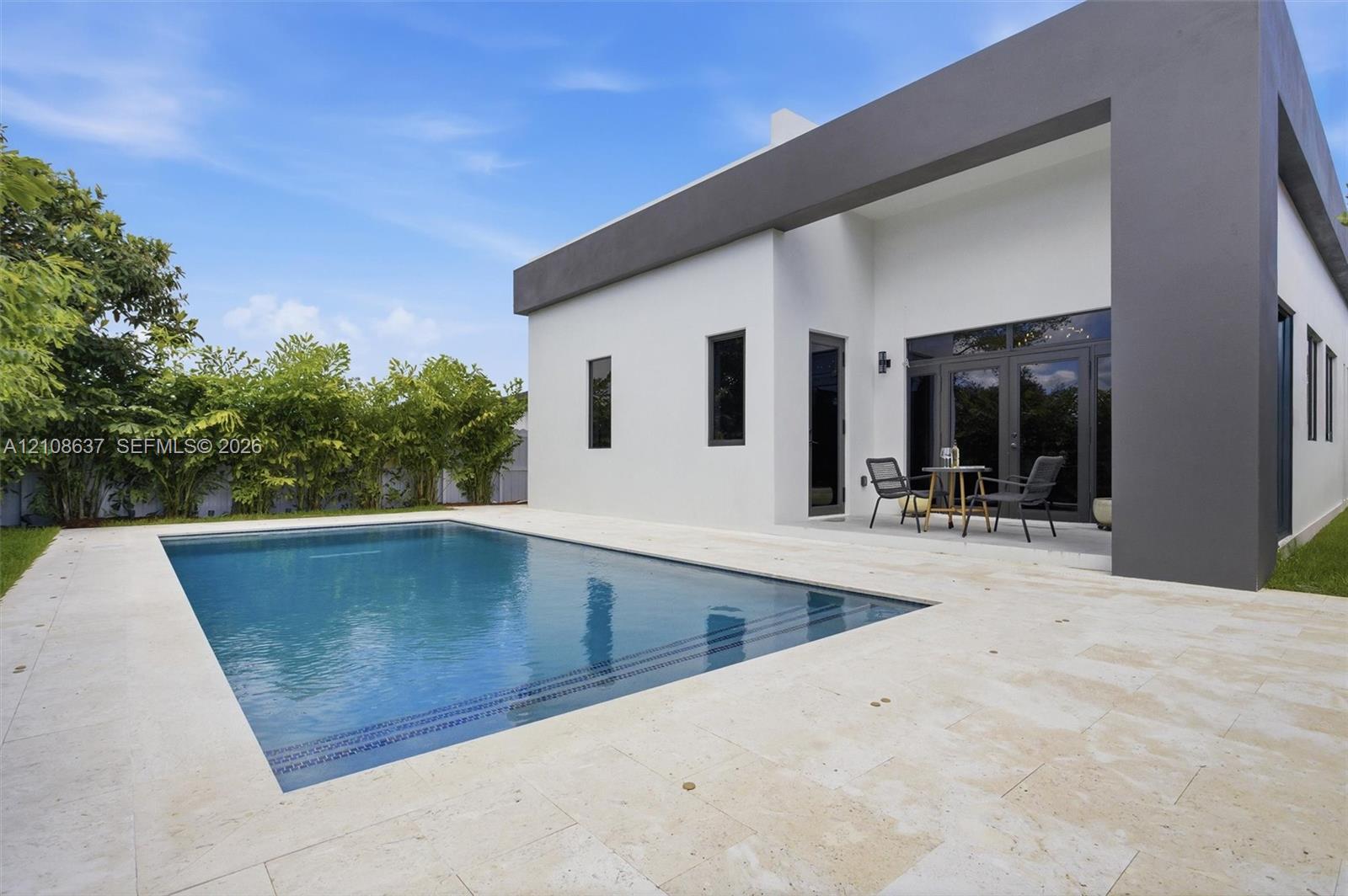 Modern exterior featuring a smooth stucco finish, rectangular swimming pool, expansive natural stone patio, and dark-toned structural framing