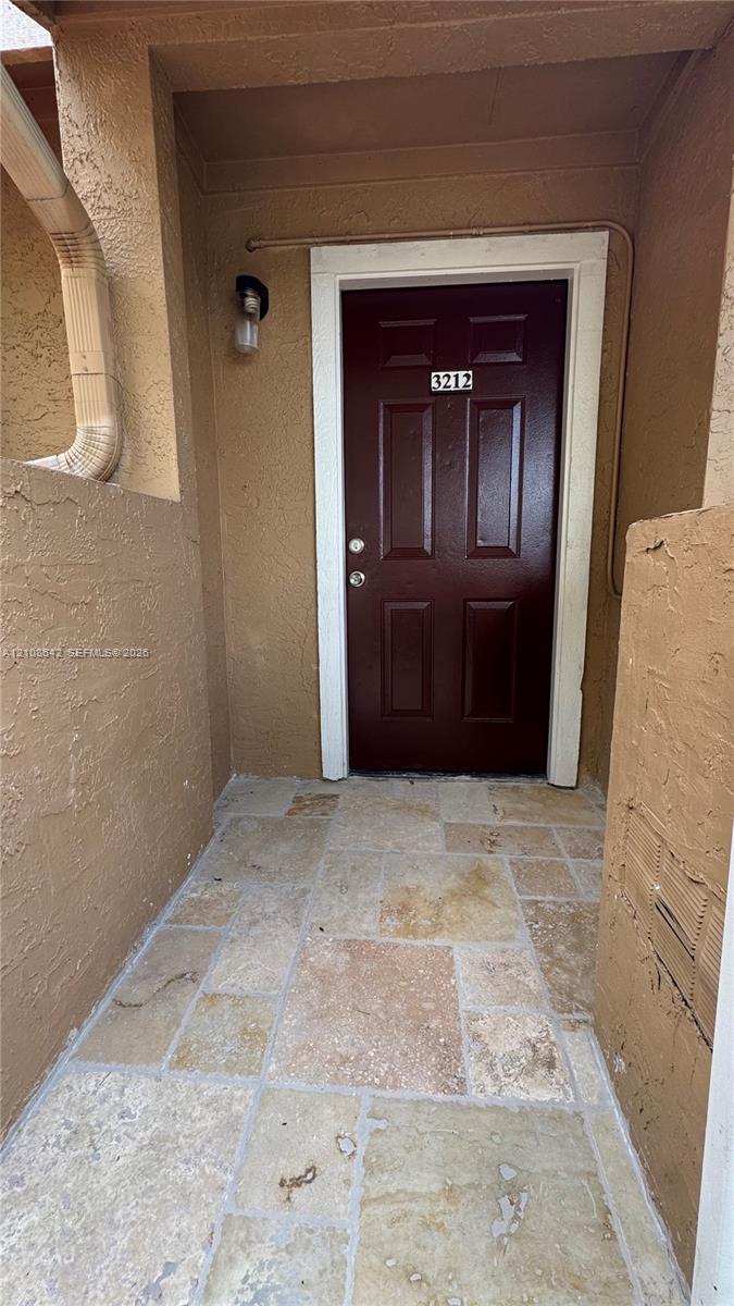 Covered entryway featuring natural stone tile flooring, a six-panel door, and a wall-mounted exterior light fixture
