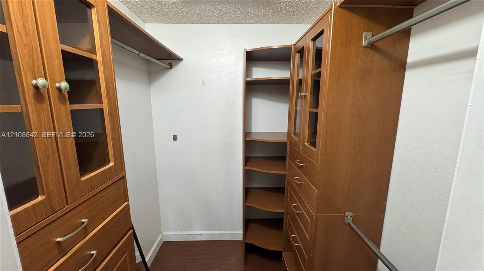 Walk-in closet featuring built-in wood-finish cabinetry, glass-paneled cabinet doors, integrated shelving, and metal hanging rods