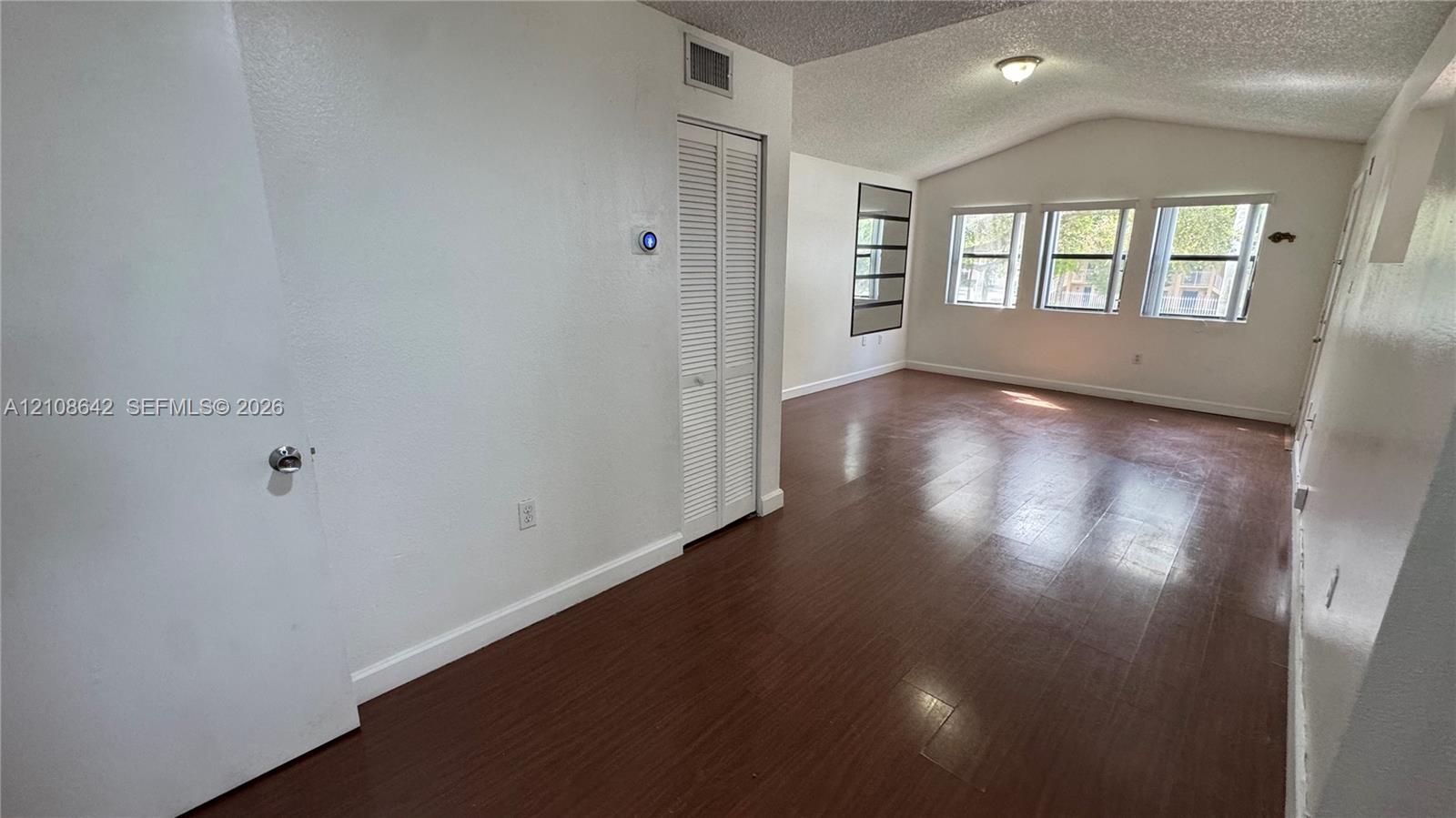Open living area featuring wood-finish flooring, vaulted ceilings, multiple windows providing natural light, and a bi-fold closet