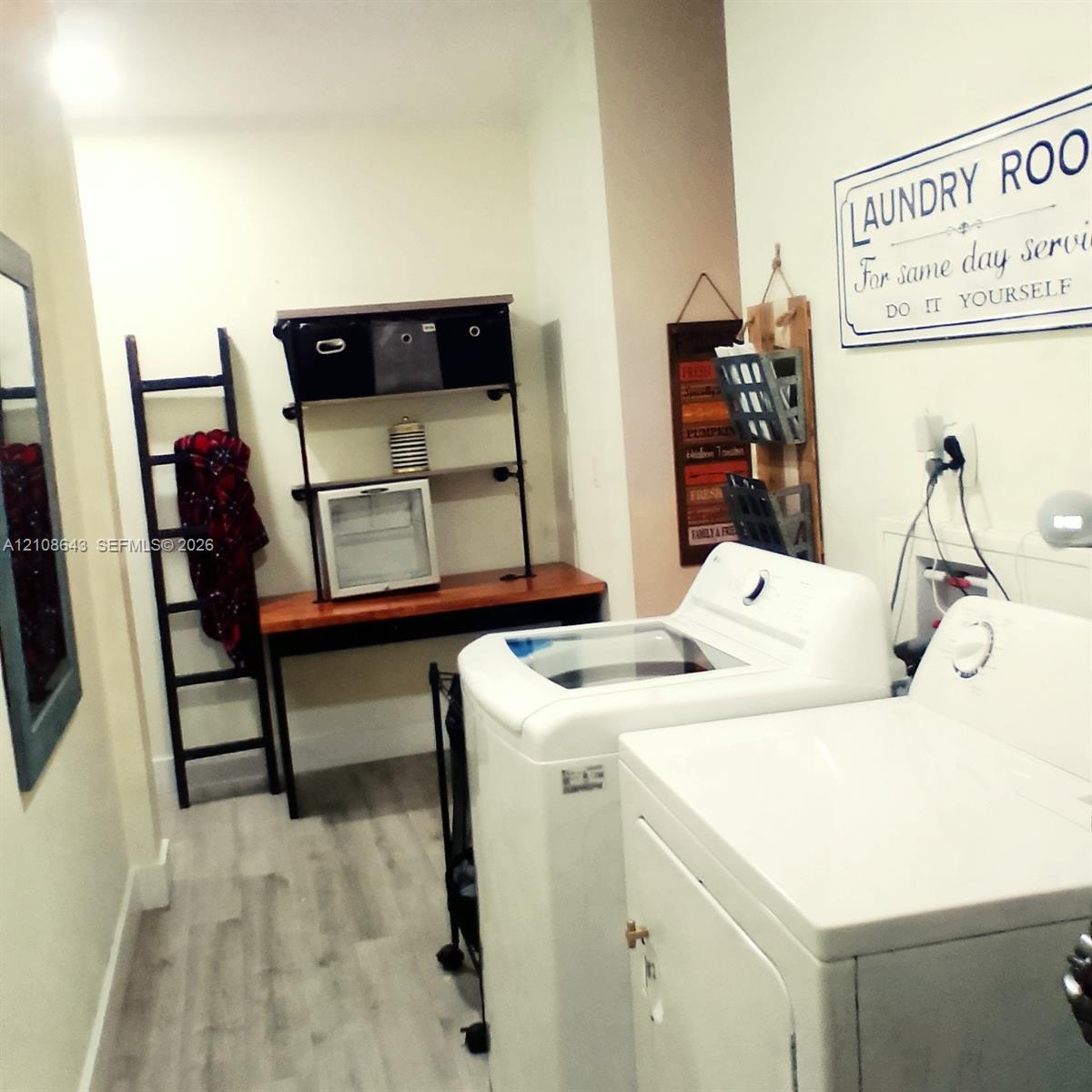 Utility space featuring wood-finish flooring, a built-in metal shelving unit with a wood-surface counter, and dedicated laundry hookups