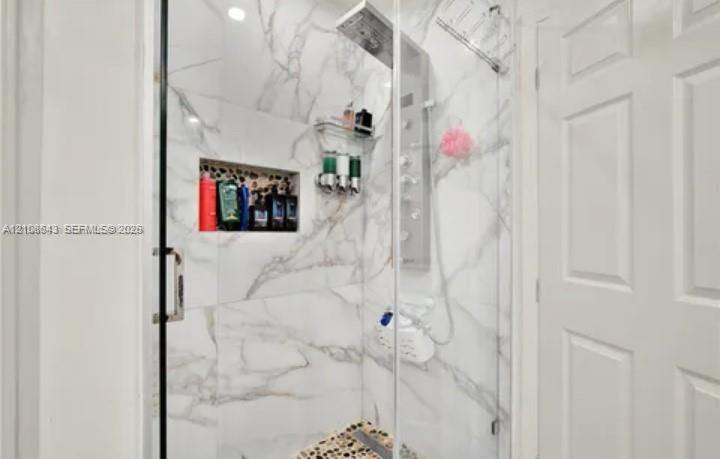Walk-in shower featuring large-format wall tile, glass enclosure, built-in recessed storage niche, multi-head shower panel system, and pebble-finish flooring
