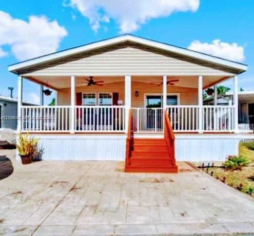 Exterior facade featuring a covered front porch with white railing, built-in ceiling fans, a stamped concrete patio, and stairs with handrails