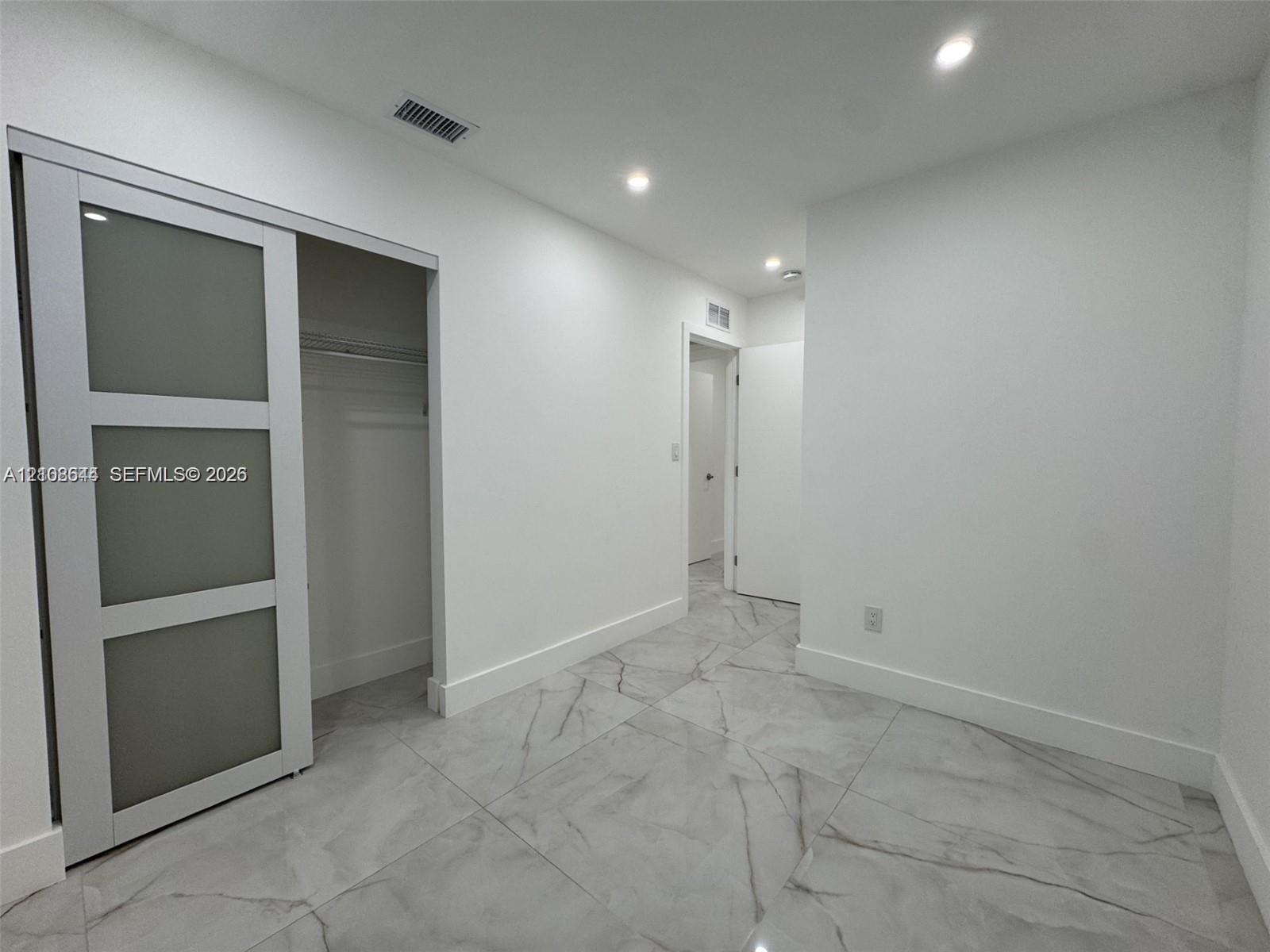 Large-format stone-style tile flooring, sliding barn door with frosted glass panels, and recessed ceiling lighting