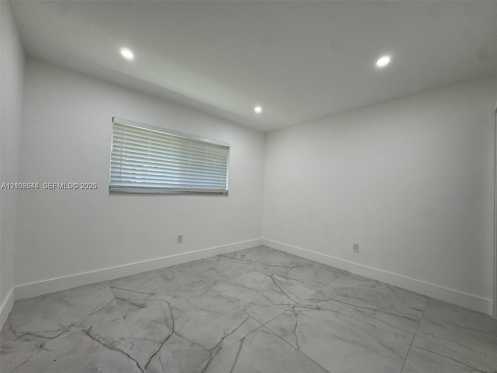 Interior room featuring large-format veined tile flooring, recessed ceiling lighting, and a single window with horizontal blinds