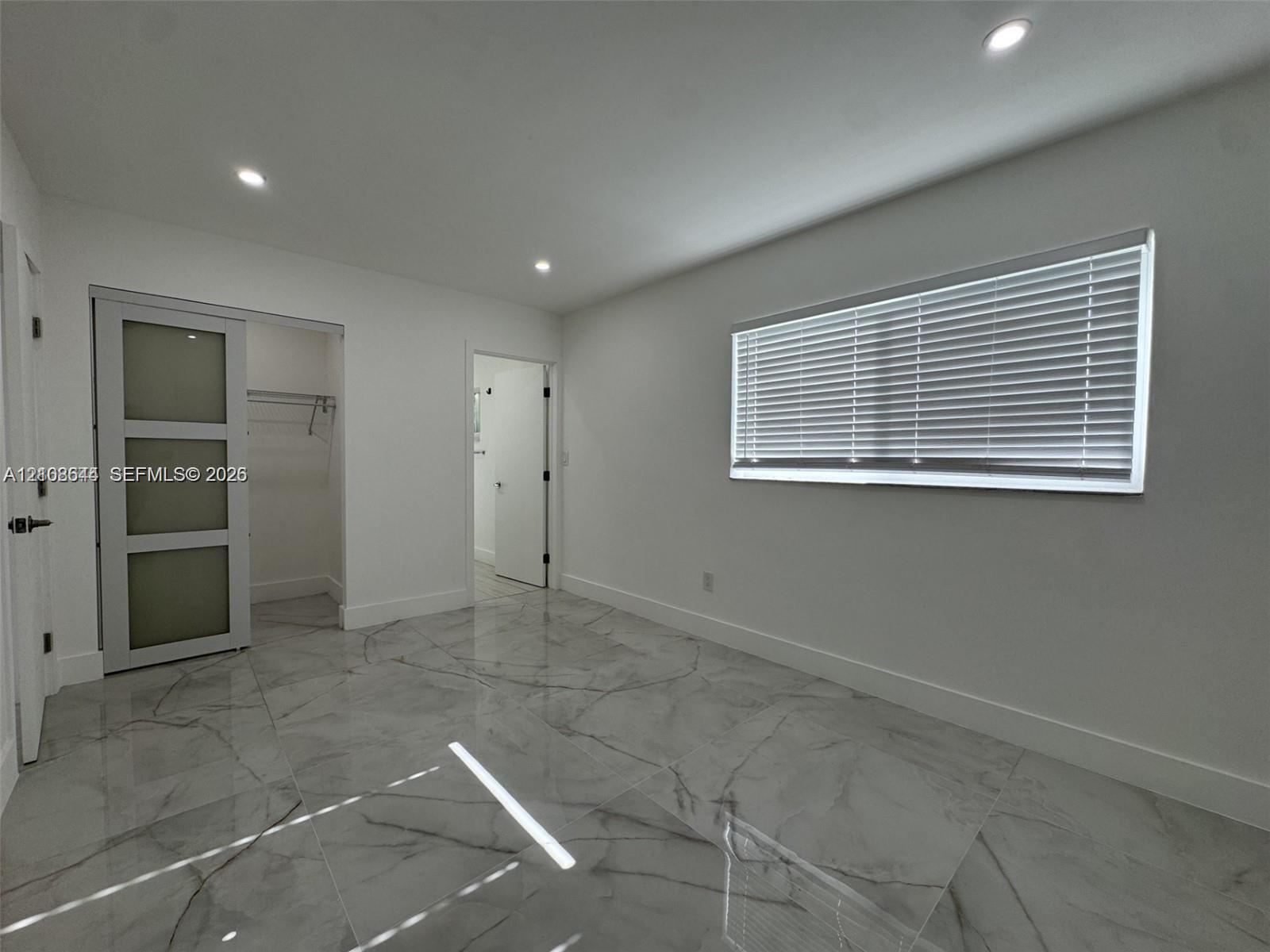 Large-format, veined tile flooring, recessed ceiling lighting, and a sliding barn-style door with frosted glass panels