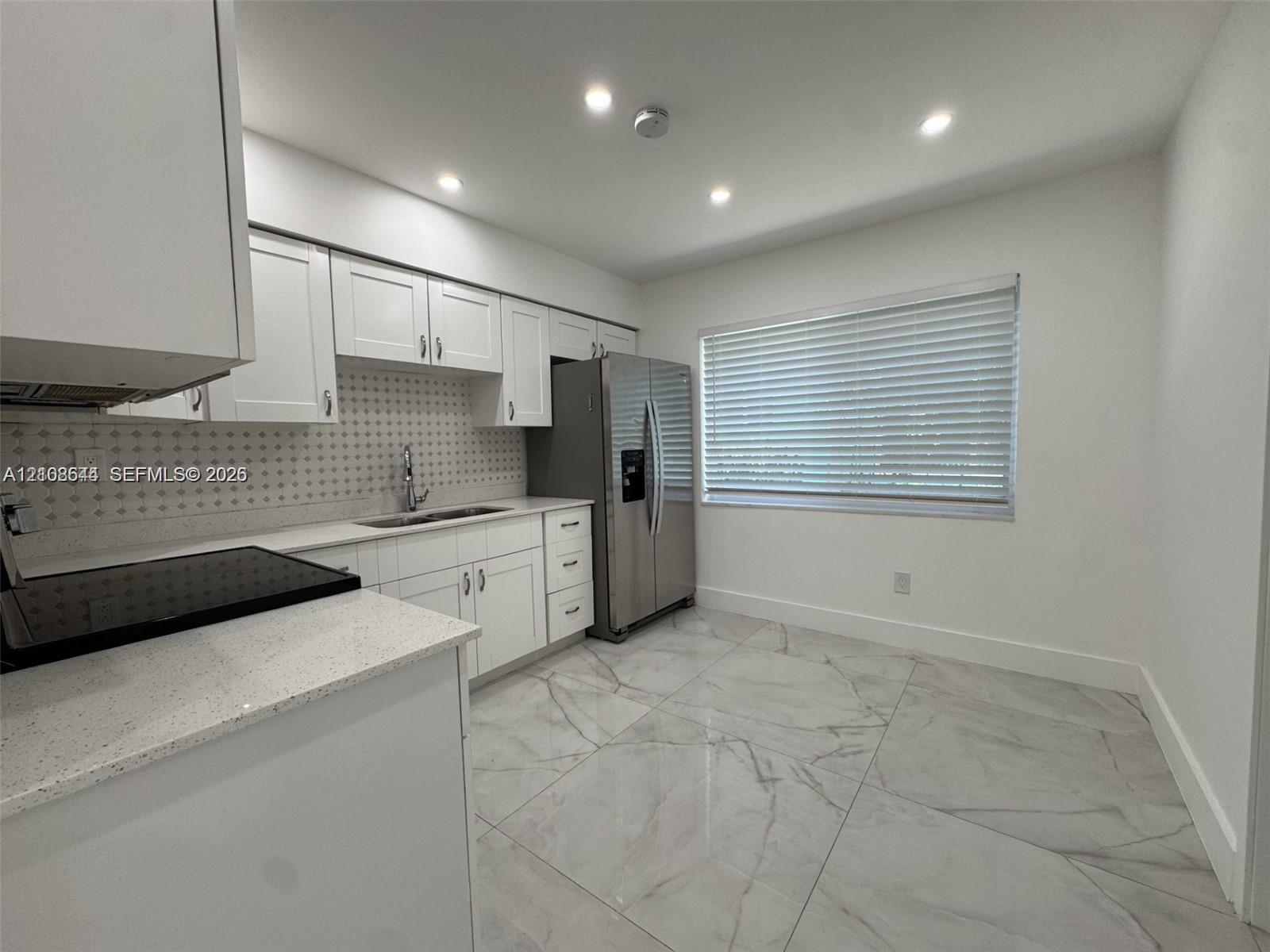 Kitchen featuring white cabinetry, quartz countertops, a patterned tile backsplash, large-format polished tile flooring, and stainless steel refrigerator