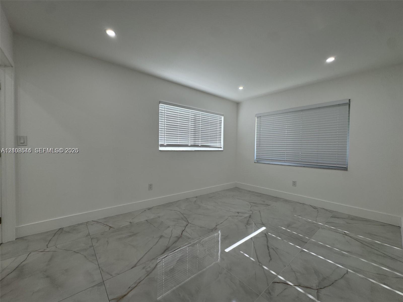 Room featuring large-format tile flooring with a veined pattern, recessed ceiling lighting, and two windows equipped with horizontal blinds