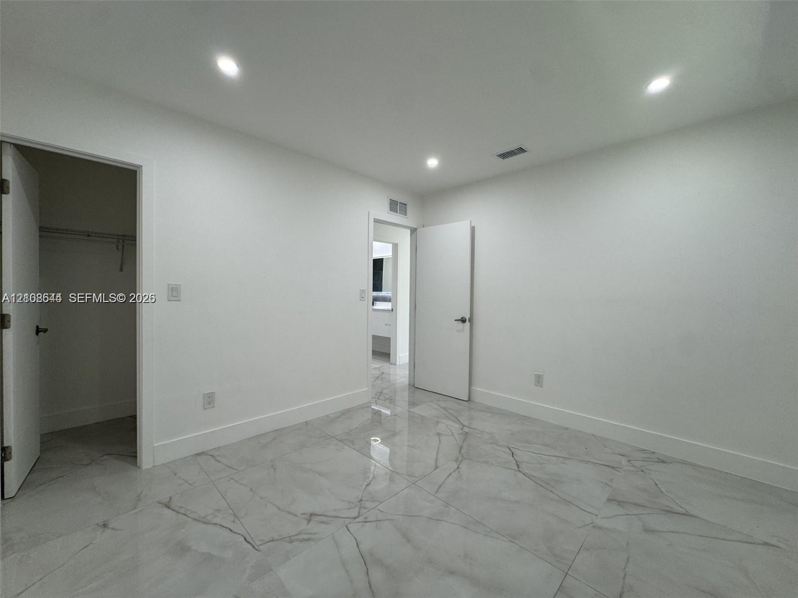 Large-format polished tile flooring with veining detail, recessed ceiling lighting, and built-in closet storage
