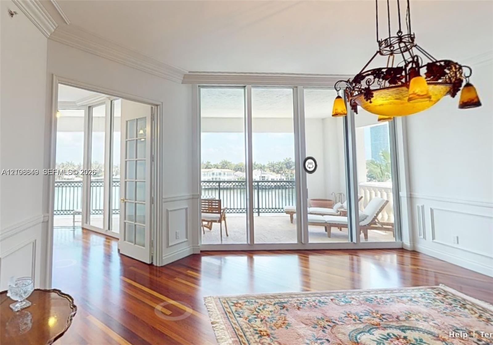 Room featuring wood-finish flooring, wainscoting, intricate crown molding, a decorative metal chandelier, and floor-to-ceiling glass panel doors