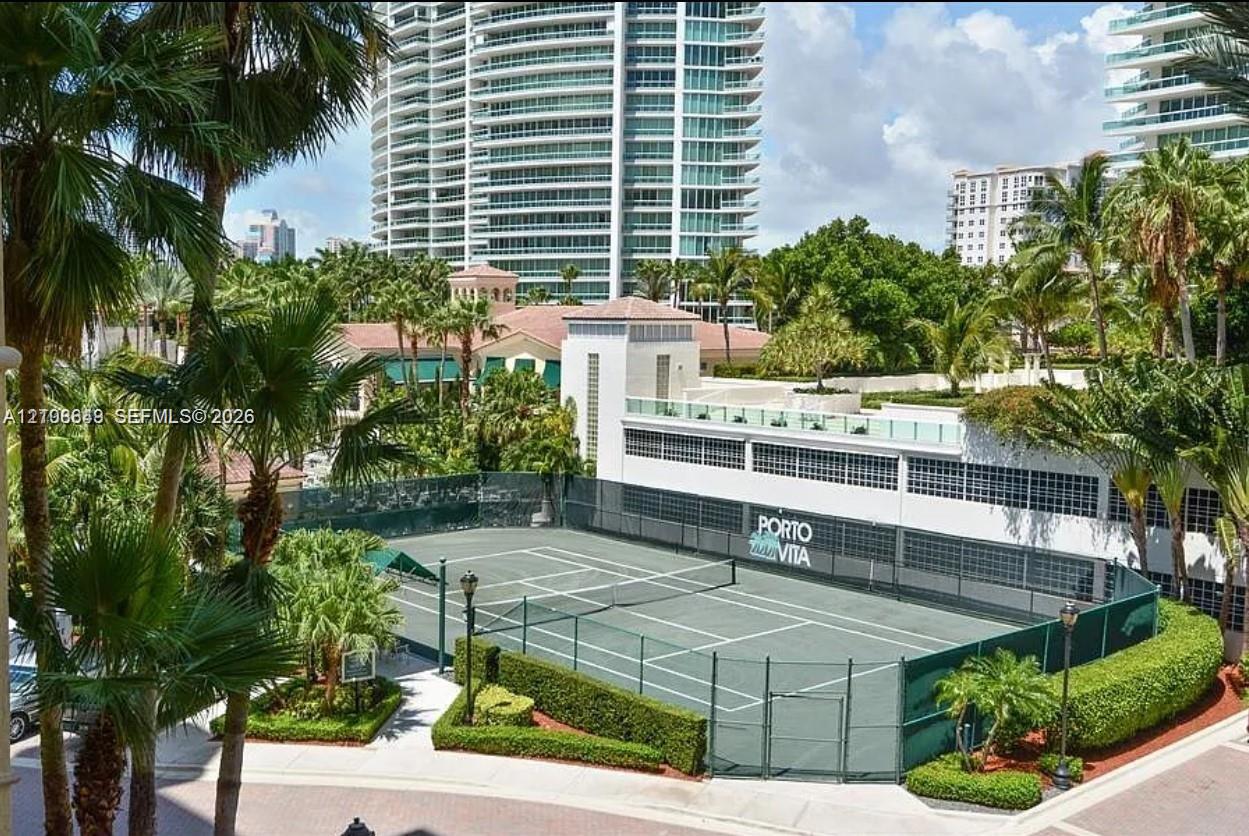 Tennis court facility featuring a fenced perimeter, hard surface, integrated lighting, and manicured landscaping