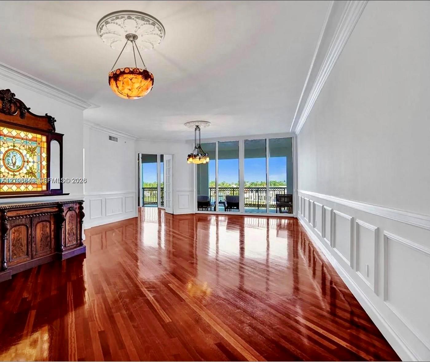 Polished wood-finish flooring, extensive wainscoting, ornate ceiling medallions, dual hanging light fixtures, and floor-to-ceiling glass sliding doors