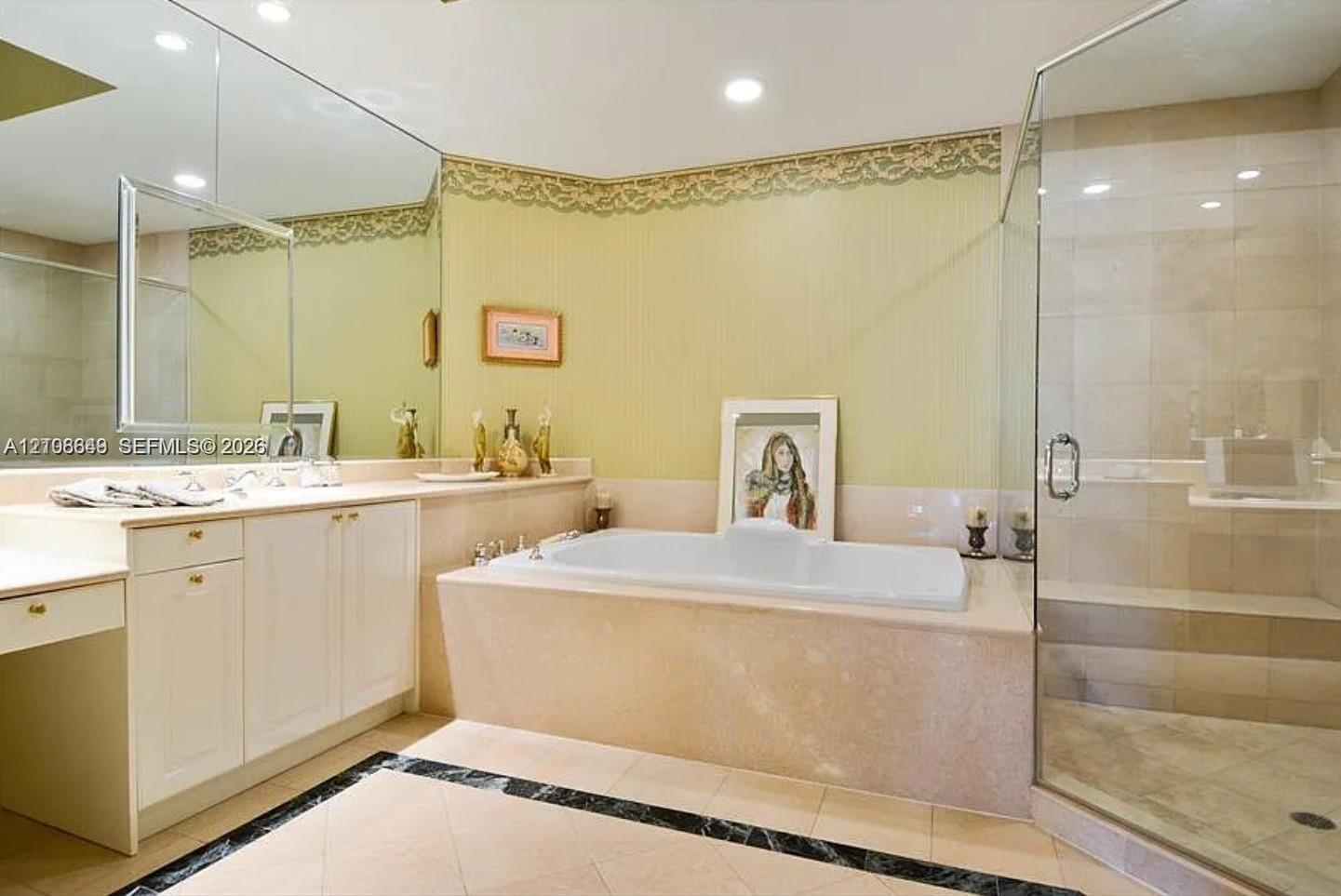 Bathroom featuring a built-in soaking tub, a frameless glass-enclosed shower with tile surround, white cabinetry, a large wall-mounted mirror, and tile flooring with a decorative border