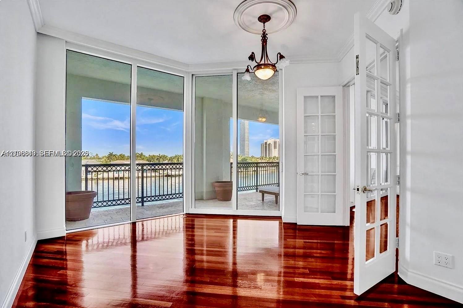 Room featuring polished wood-finish flooring, floor-to-ceiling glass paneling, a decorative ceiling medallion with an attached chandelier, and French-style interior doors