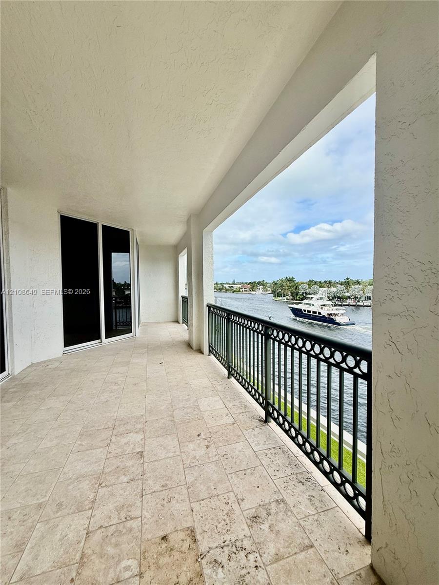 Covered balcony featuring stone tile flooring, a decorative metal railing, and direct water exposure