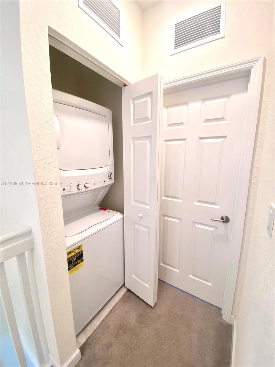 Stackable laundry appliance set housed in a recessed closet with a paneled door, featuring neutral wall finishes and carpeted flooring