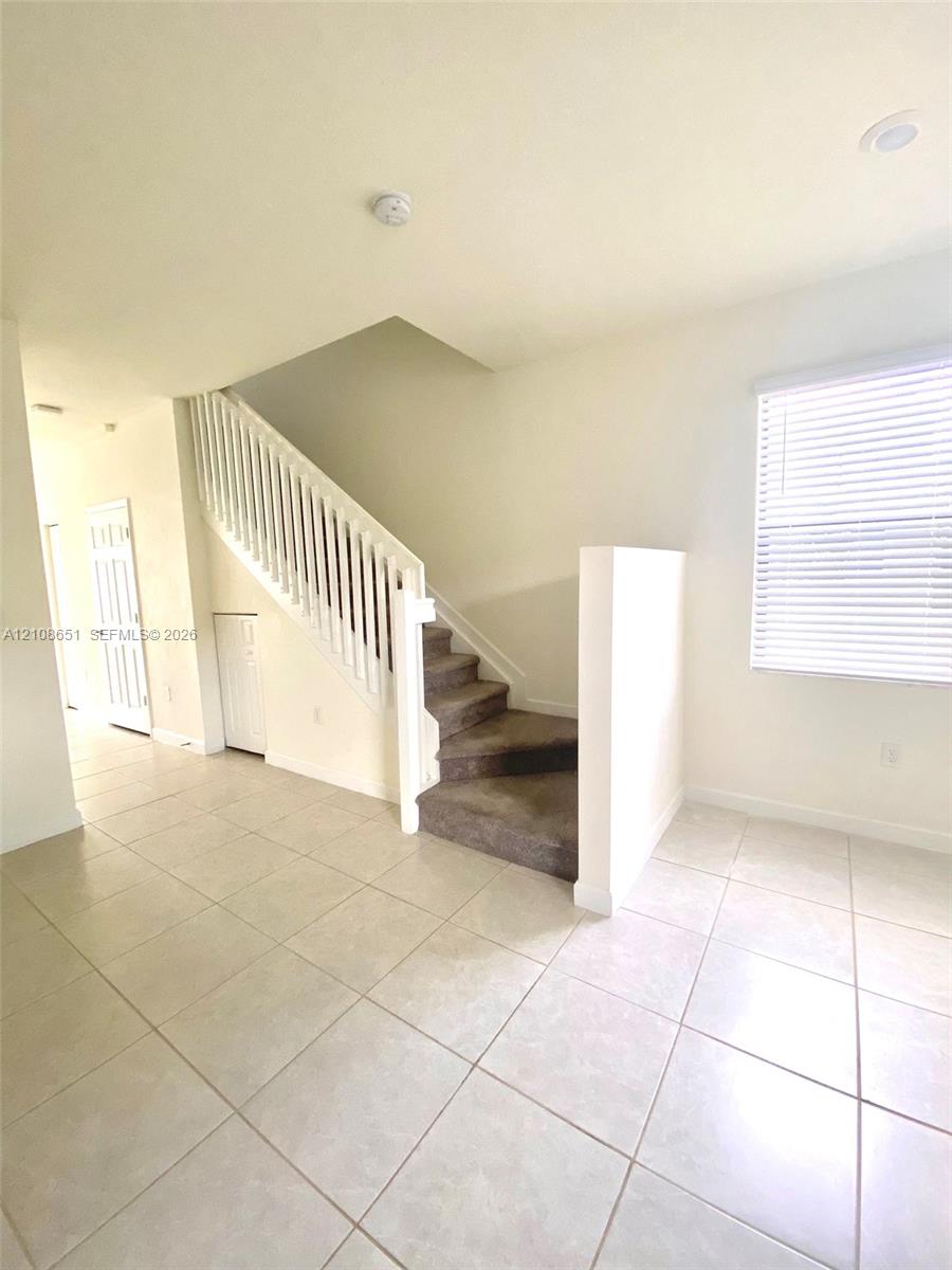 Staircase featuring a white balustrade, carpeted steps, and large-format tile flooring