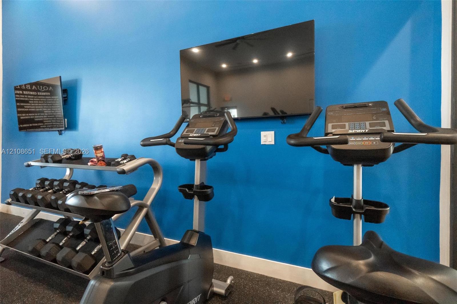 Fitness center featuring wall-mounted television, rubberized flooring, and recessed ceiling lighting